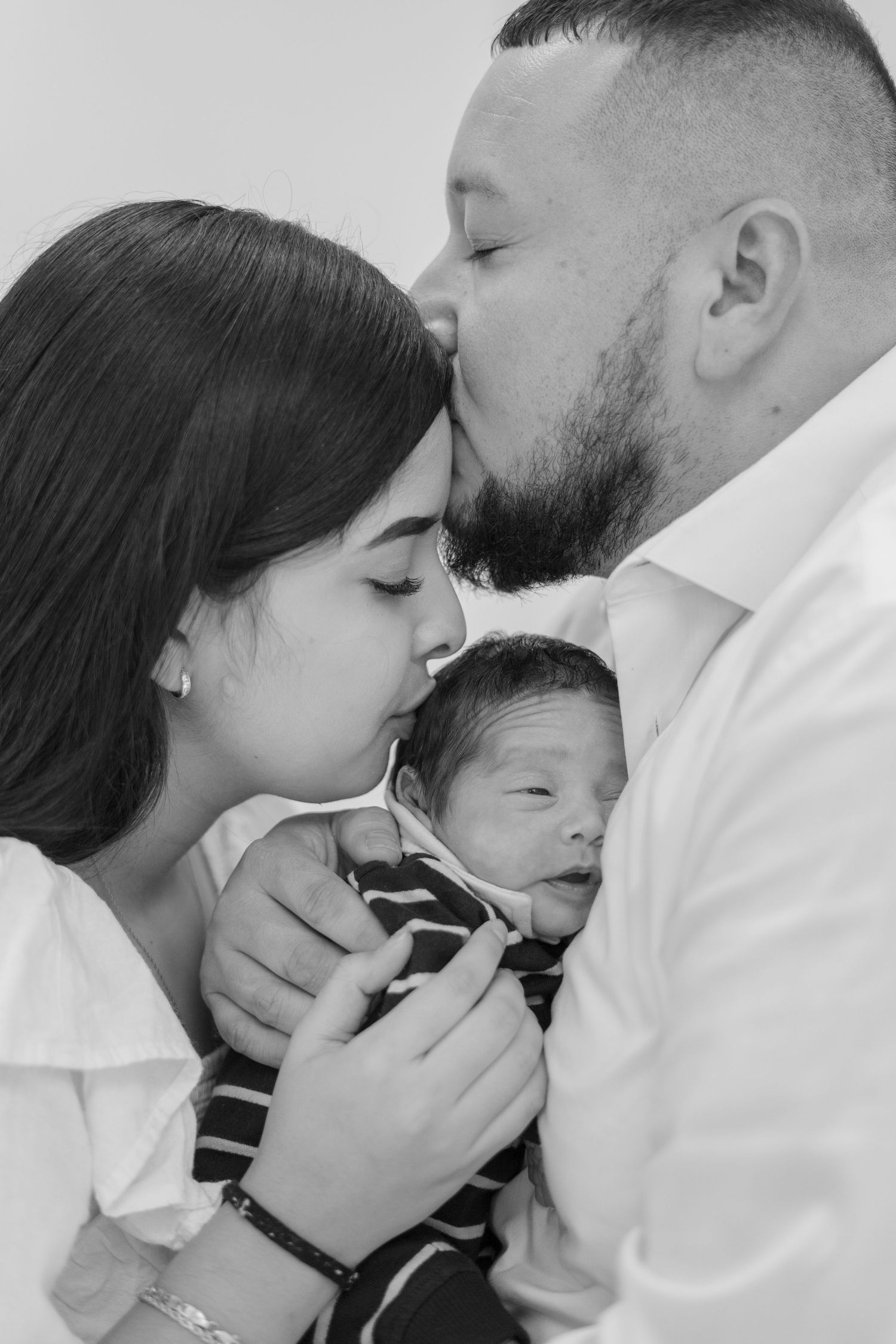 Black and white photo of new parents kissing their newborn baby.