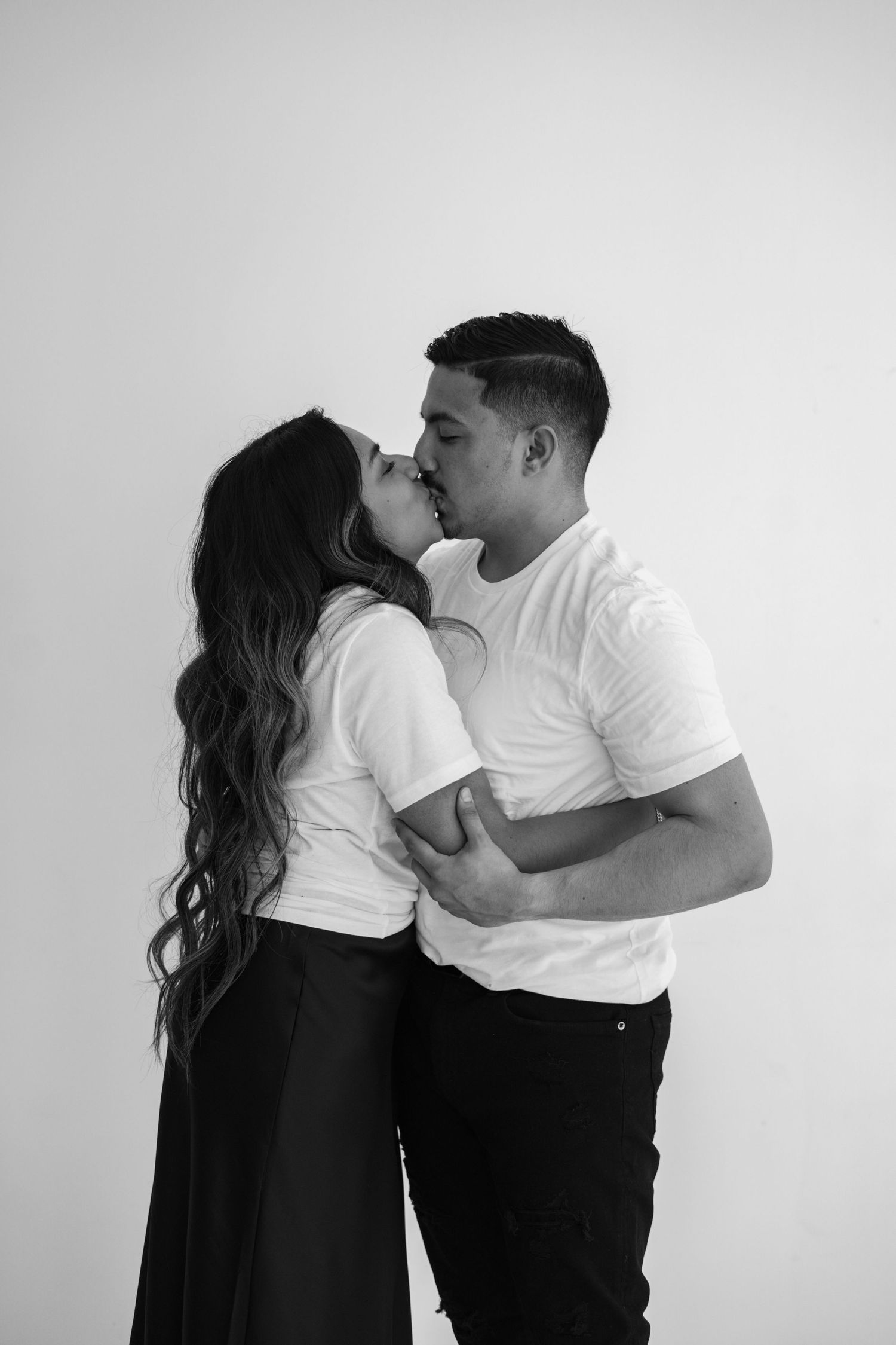 Black and white romantic photo of couple sharing a kiss against a white studio background.