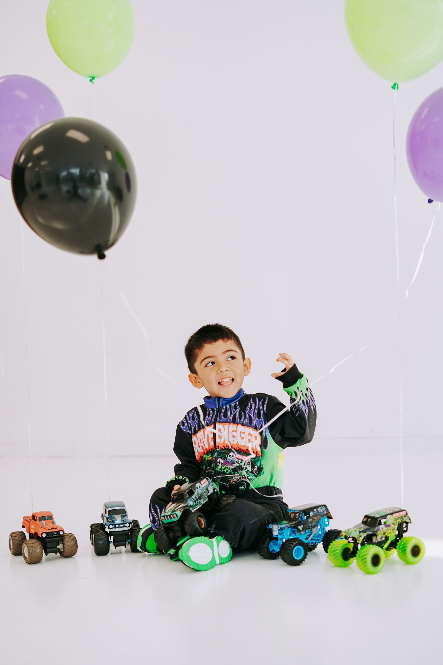 Young boy in Grave Digger costume celebrating birthday with monster trucks and colorful balloons.