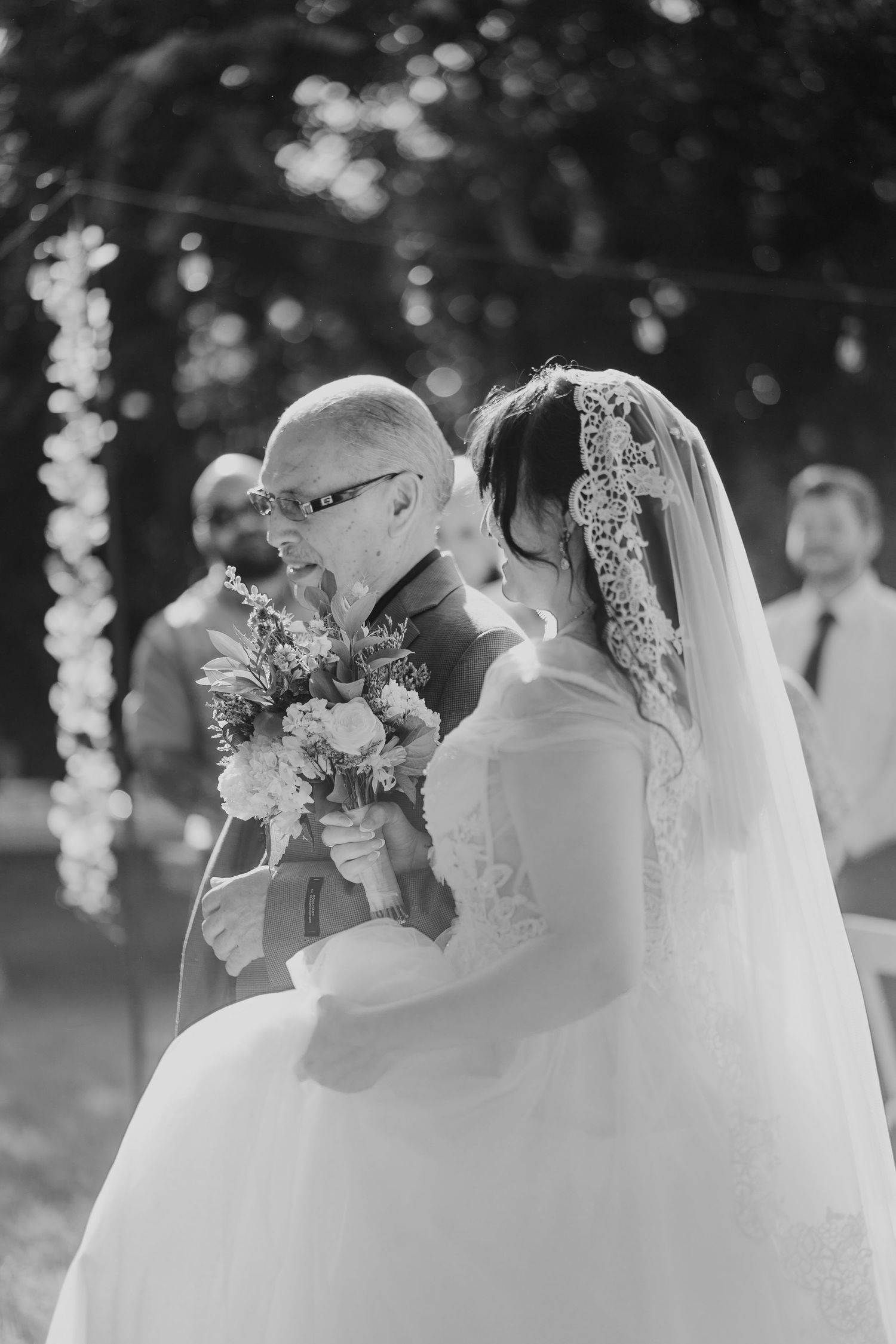 Black and white photo of a father walking his bride daughter down the aisle at an outdoor wedding ceremony.