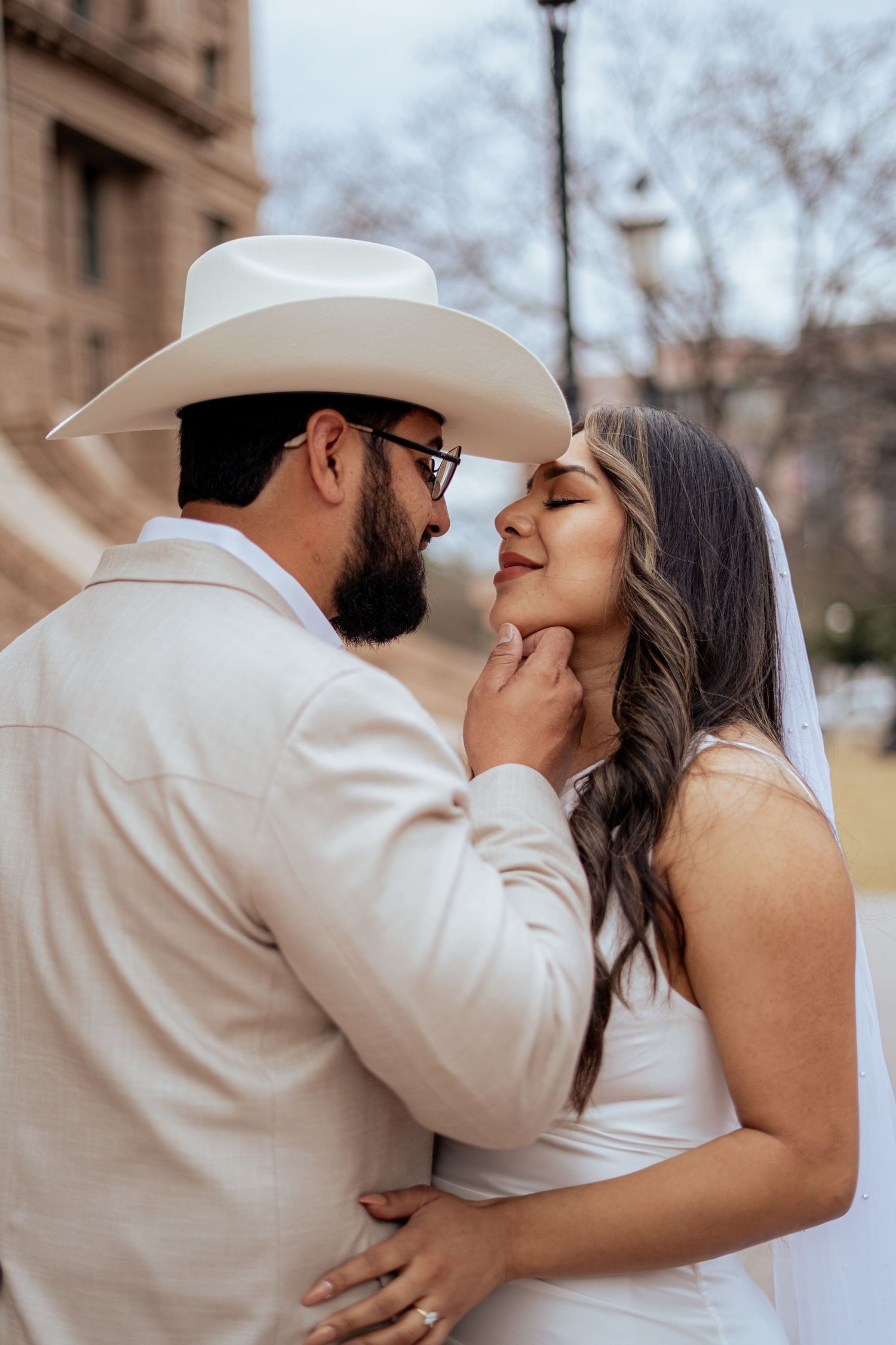 Groom in white cowboy hat tenderly holds bride's chin as they share an intimate moment on wedding day.