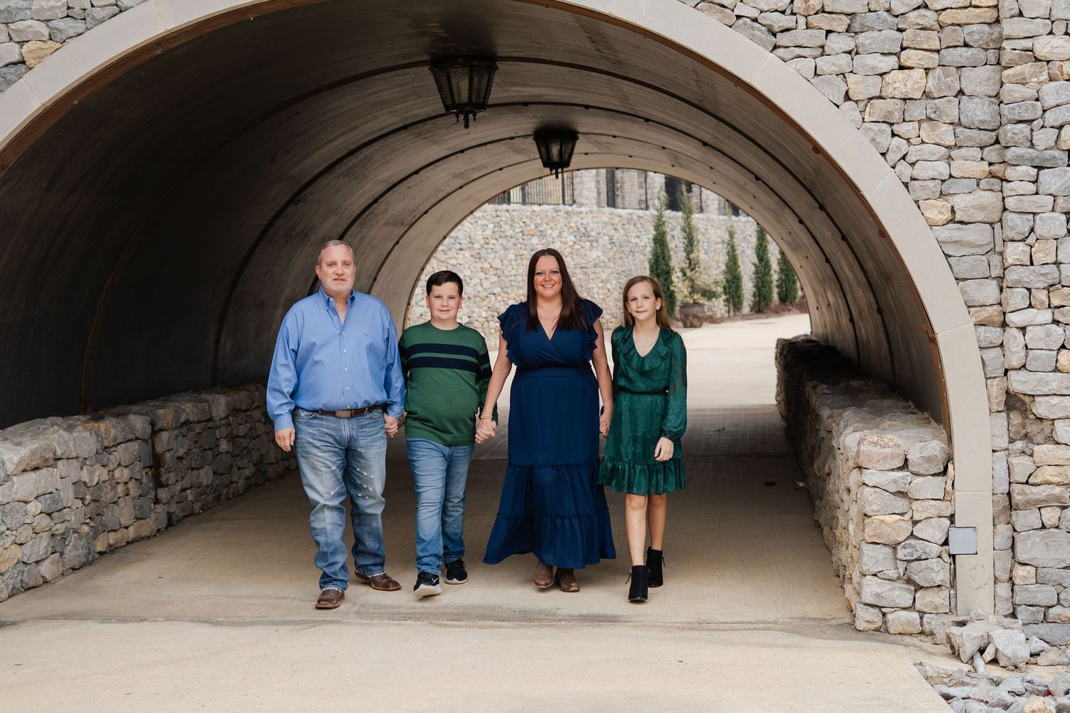 A family of four walks together through a stone tunnel archway at a scenic outdoor location.