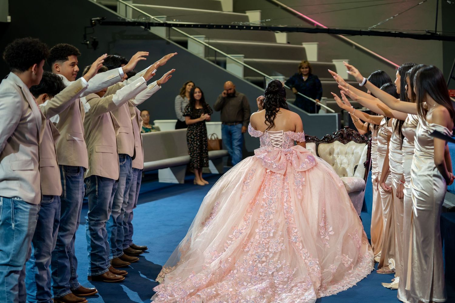 Quinceañera in pink gown walks through an arch of outstretched hands during her celebration ceremony.