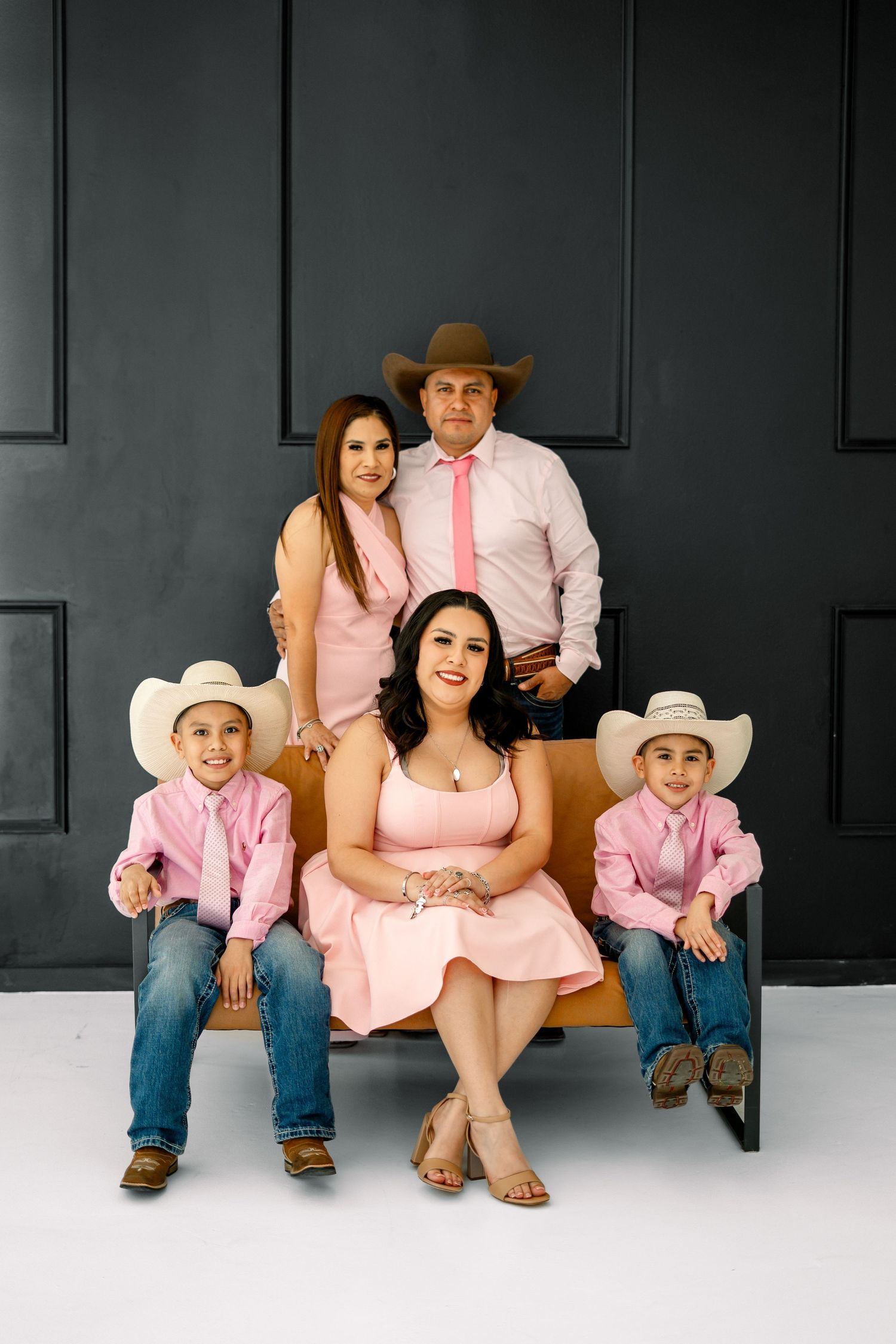 Family of five in pink western outfits with cowboy hats in a studio portrait.