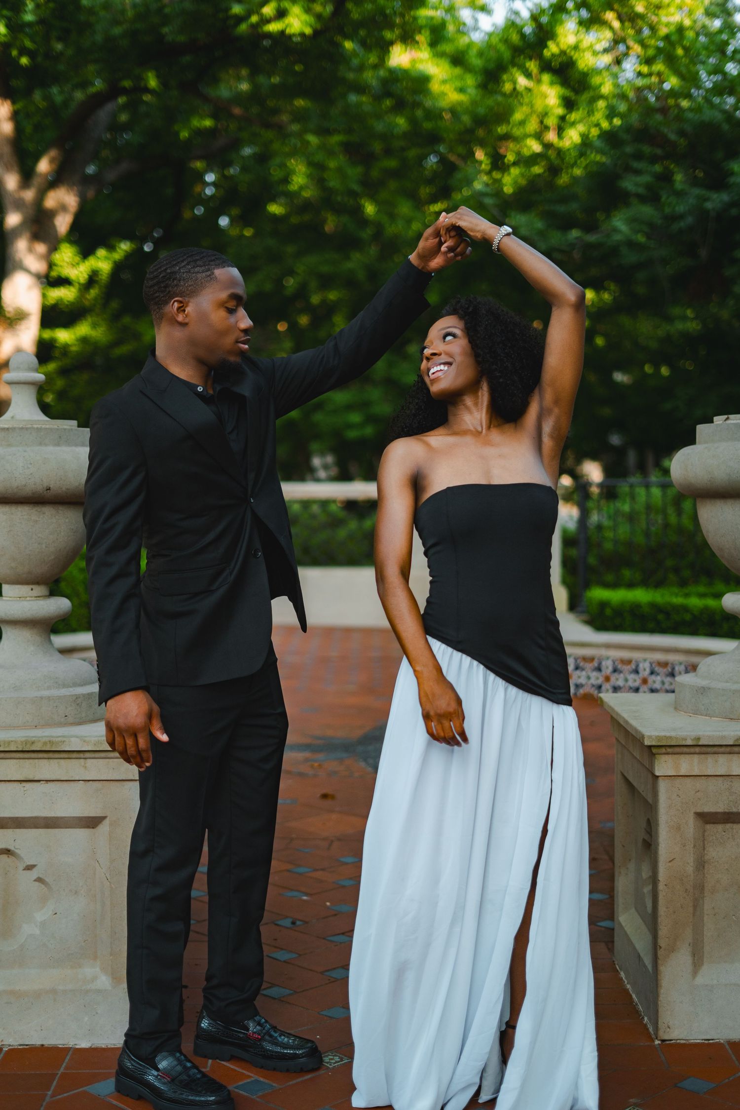 Stylish Black couple dancing outdoors, man spinning woman in black and white formal wear.