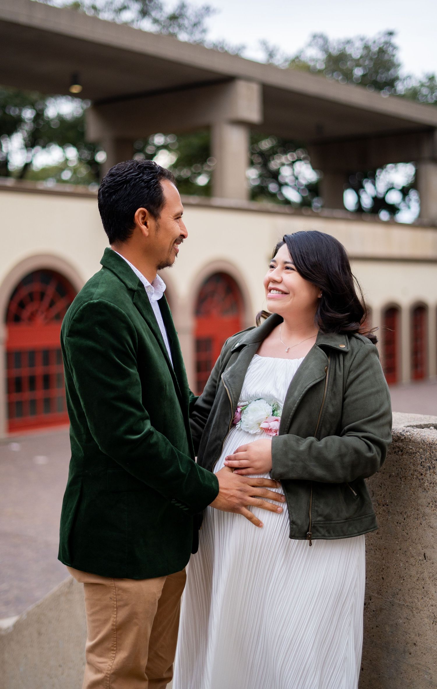 Expecting couple laughing together during maternity photo shoot at outdoor venue with red arches.