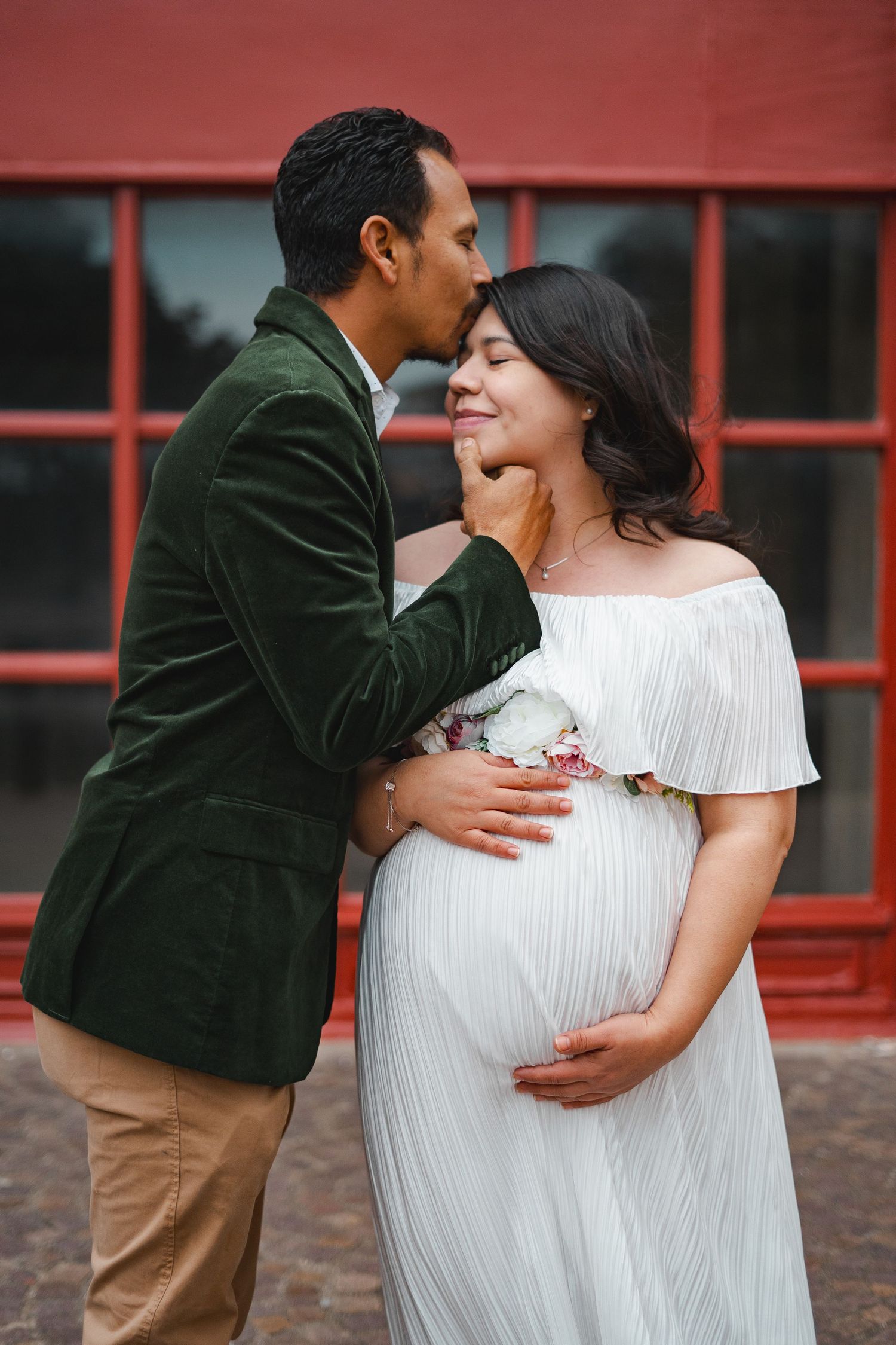 Couple sharing tender moment during maternity photo shoot, man kissing pregnant womans cheek.