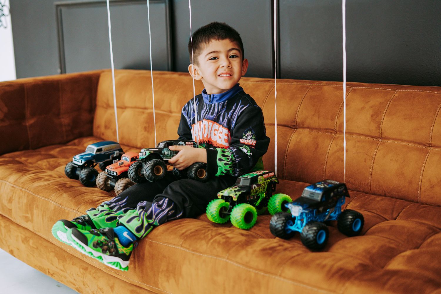 Back view of boy in Grave Digger racing suit with monster truck graphic near orange sofa.
