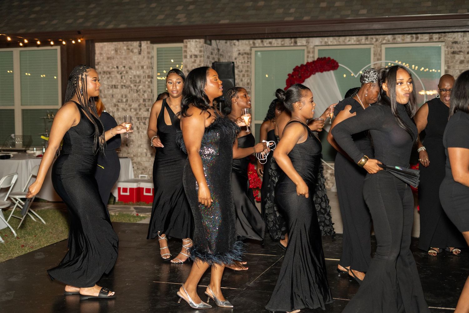 Wedding guests in elegant black gowns dancing together on the reception dance floor at night.
