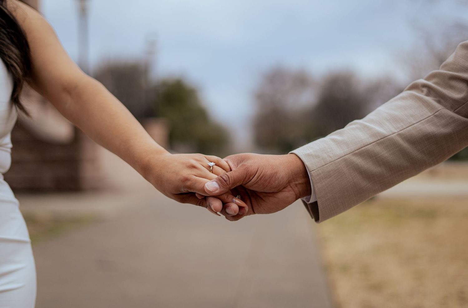 Close-up of bride and groom holding hands showing wedding ring during outdoor wedding portraits.
