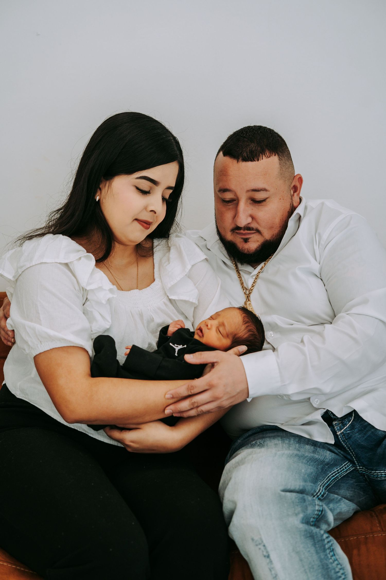 New parents gaze lovingly at their sleeping newborn baby dressed in a black outfit.