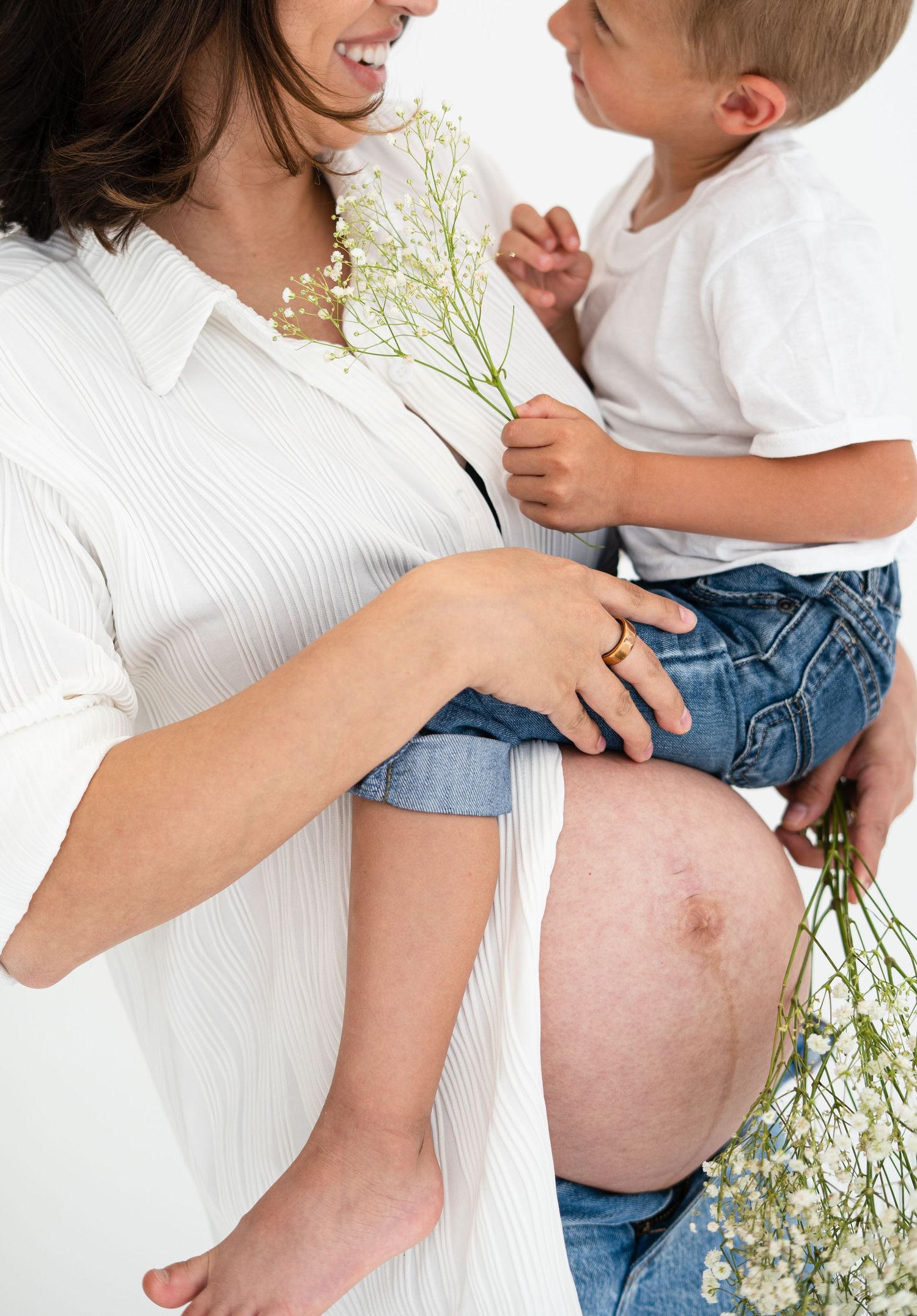 Pregnant woman in white shirt holding child with baby's breath flowers against white background.