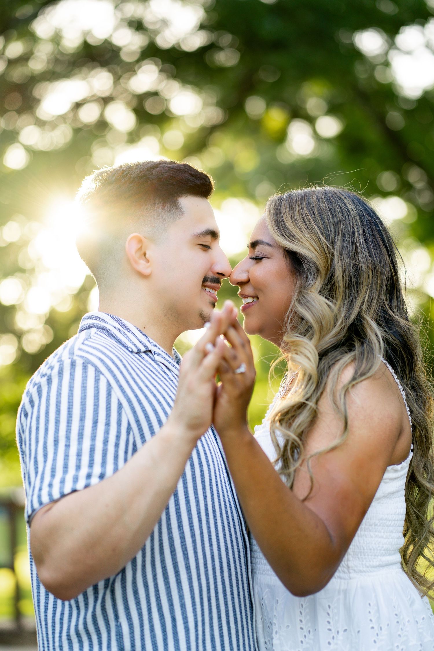 Happy couple about to kiss while holding hands with golden sunlight glowing behind them outdoors.