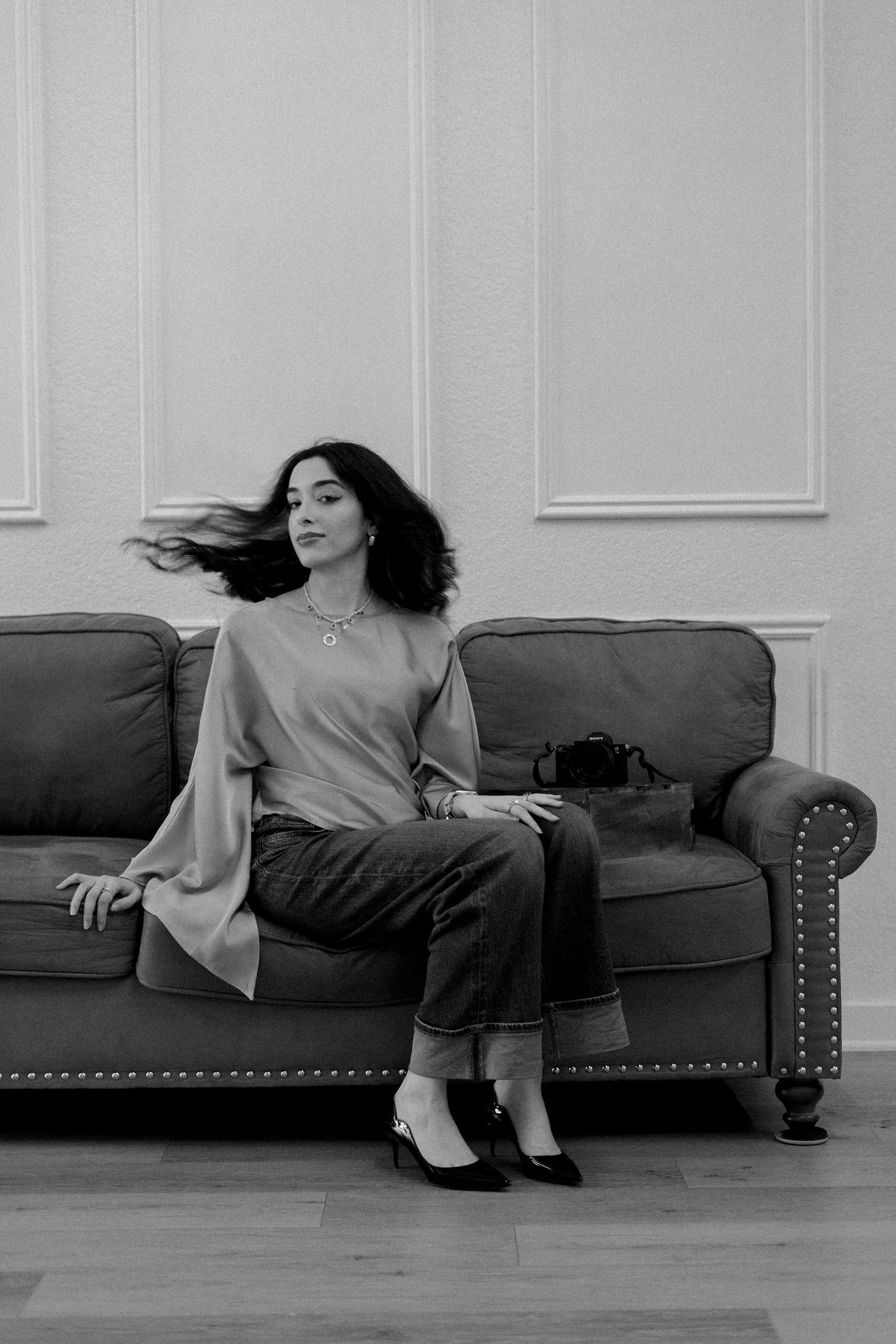 Black and white photo of a woman with flowing hair sitting gracefully on a tufted sofa in an elegant room.