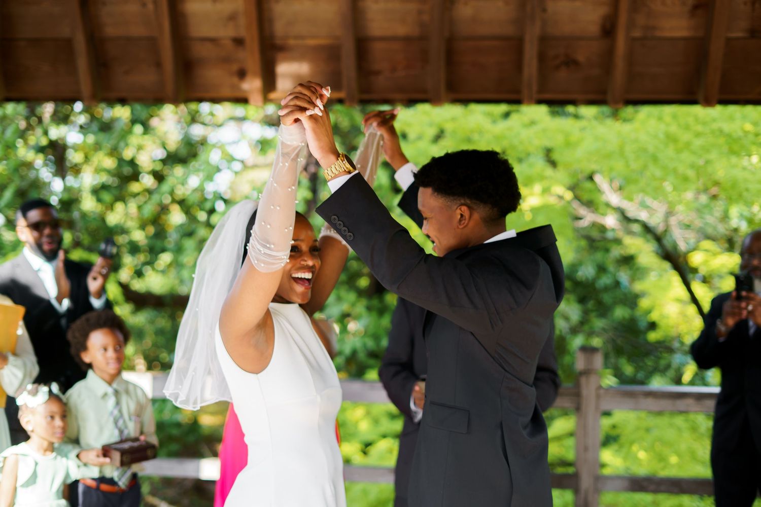 Joyful newlyweds share first dance under wooden pavilion as groom twirls bride in short white wedding dress.