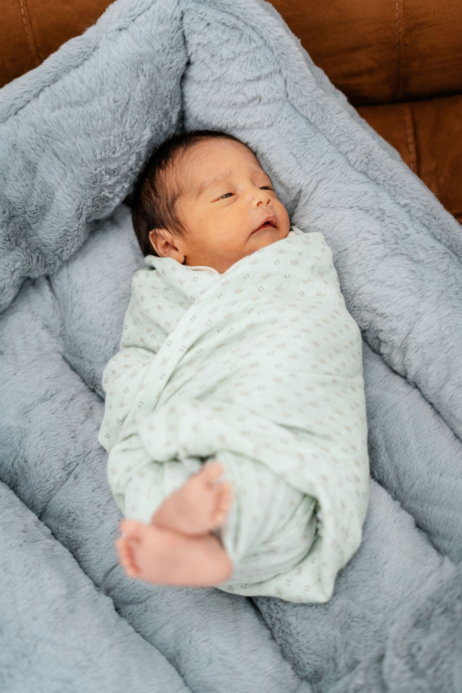 Peaceful newborn baby swaddled in a green blanket lying on a soft blue fluffy surface.