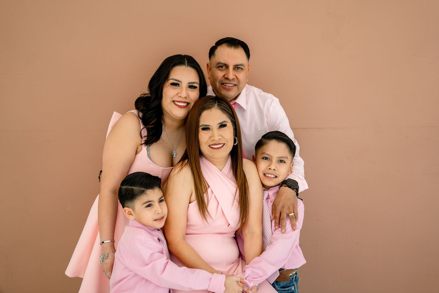 Family of five in pink coordinated outfits smiling together in a studio.