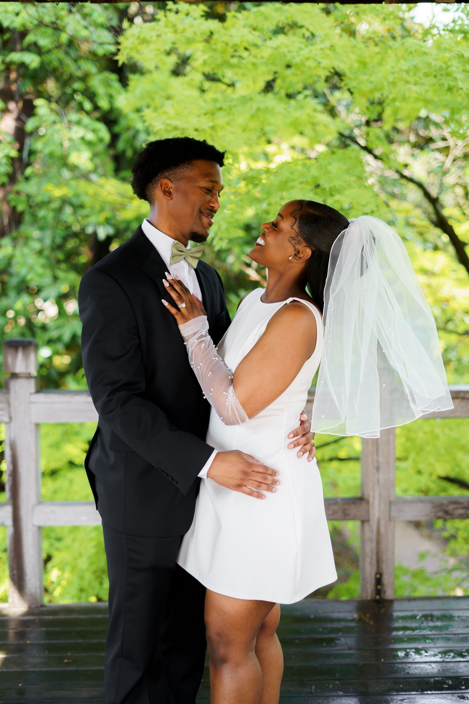 Newlyweds embrace and smile at each other on a rainy day, bride in short white dress with veil.