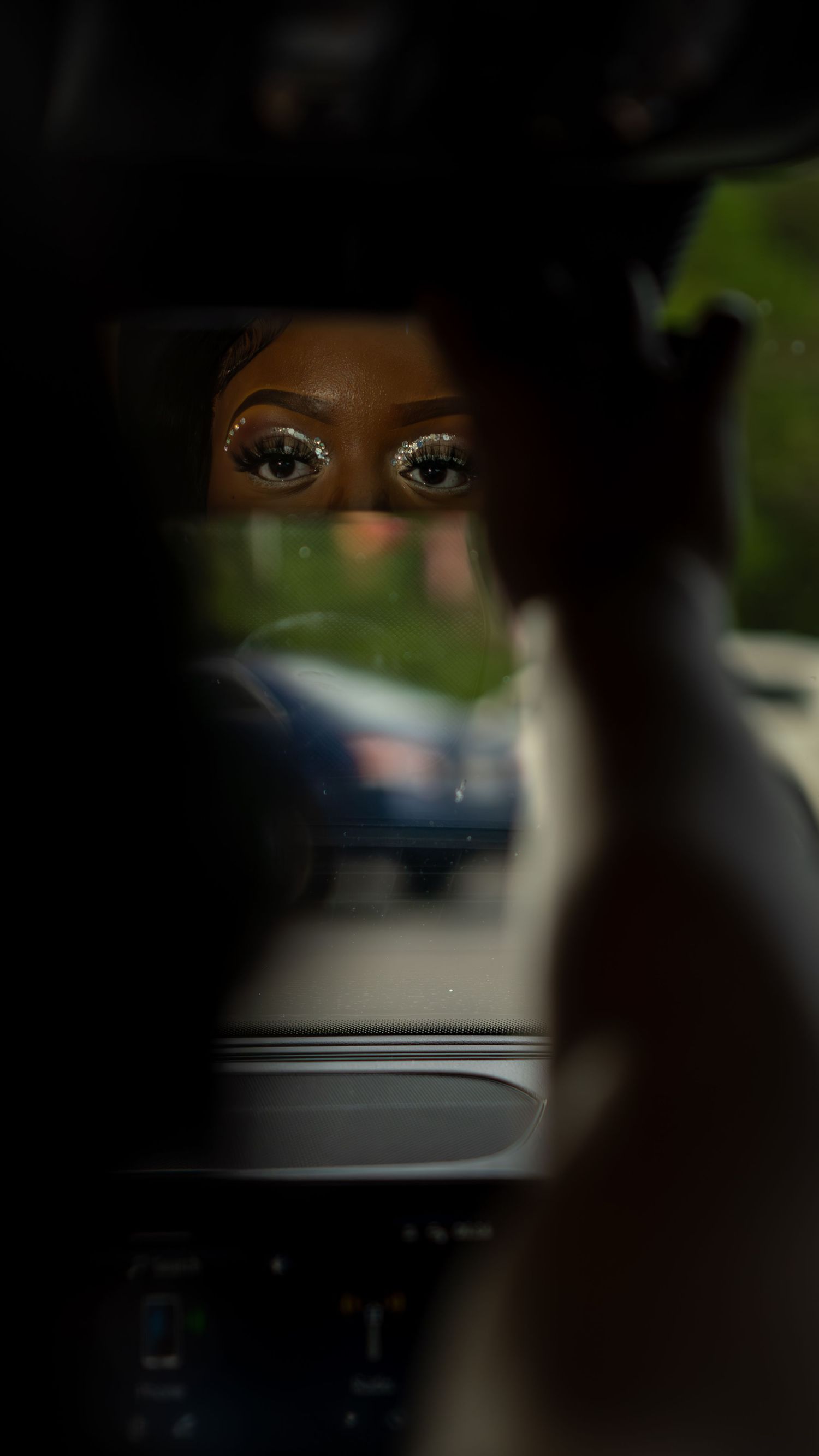 Artistic close-up shot through car window showing reflected eyes in rearview mirror.