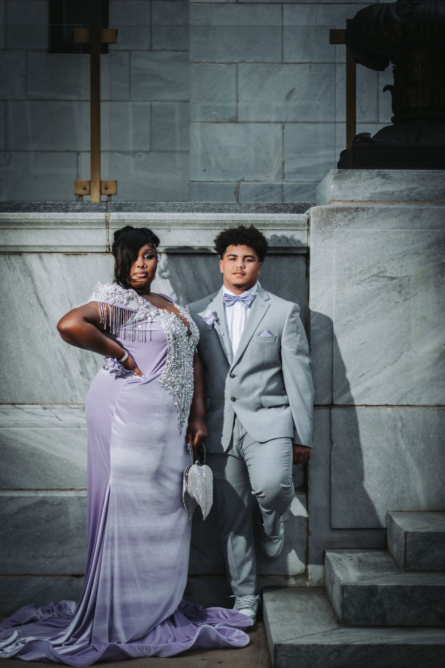 Elegant wedding portrait against stone wall featuring lavender dress and gray suit.