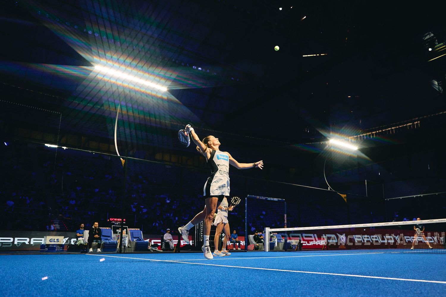 Fotografia esportiva de tennis en pista nocturna amb jugador realitzant servei potent