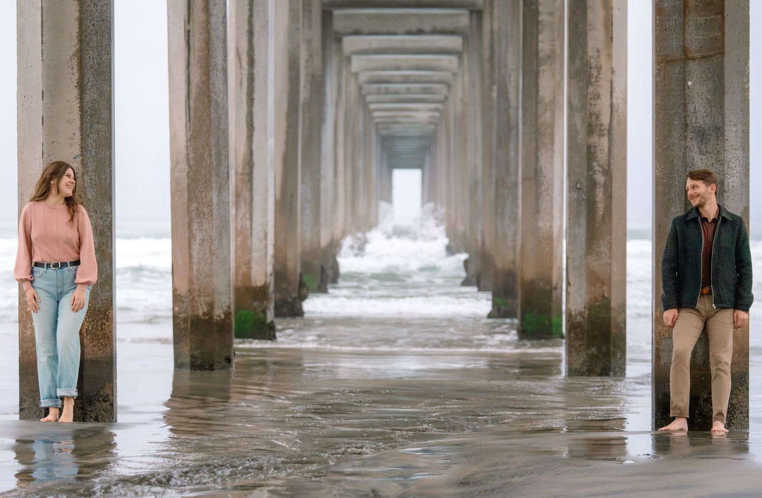 Couple standing under ocean pier during a romantic engagement photography session captured by a Colorado couples photographer.