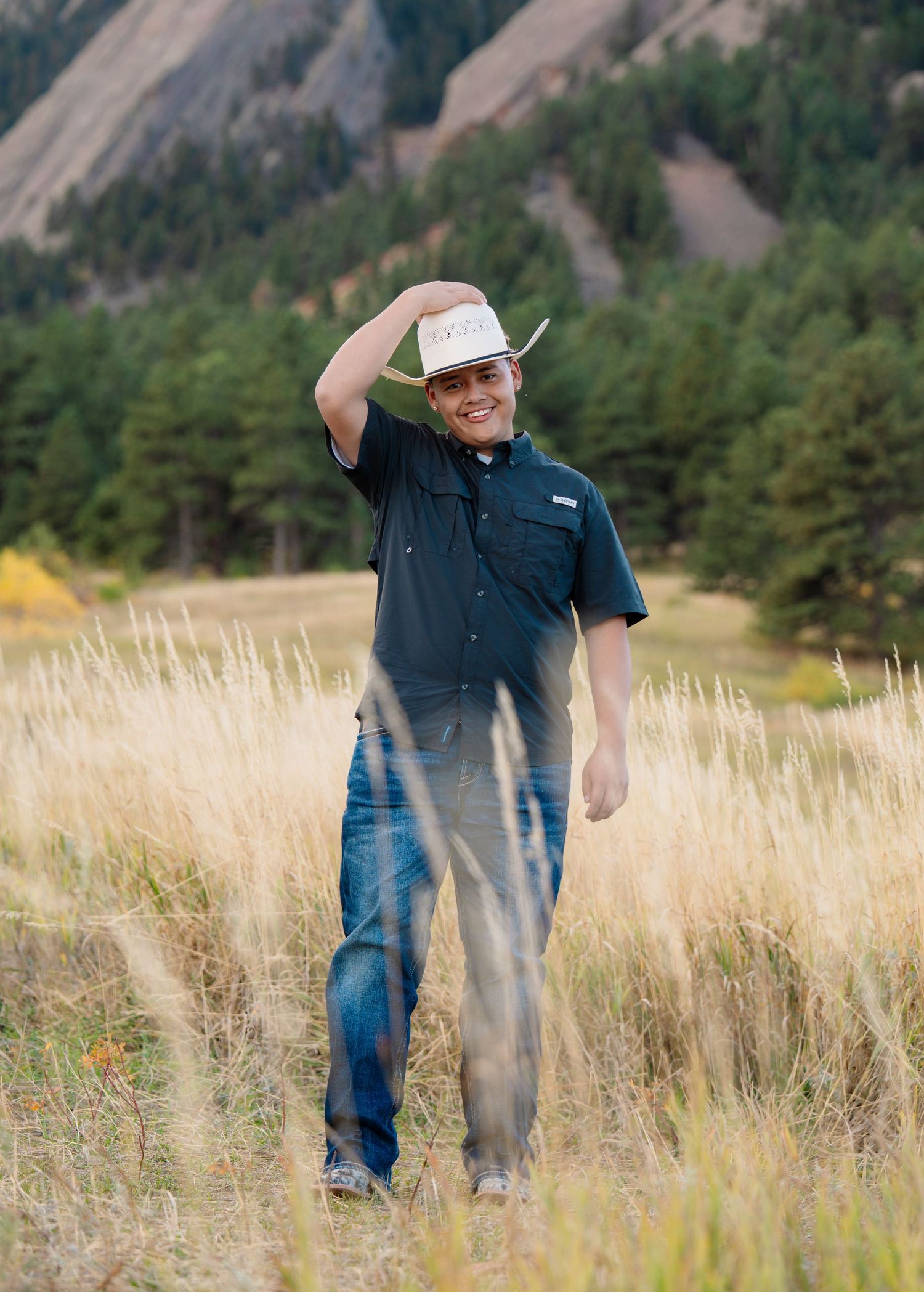High school senior portrait in golden field with mountain backdrop during an outdoor Colorado senior photography session.