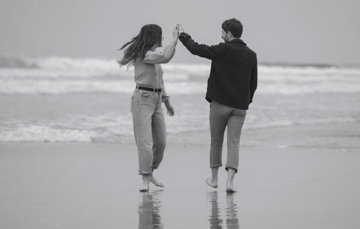 Couple dancing along shoreline during a playful beach engagement photography session captured by a Colorado couples photographer.