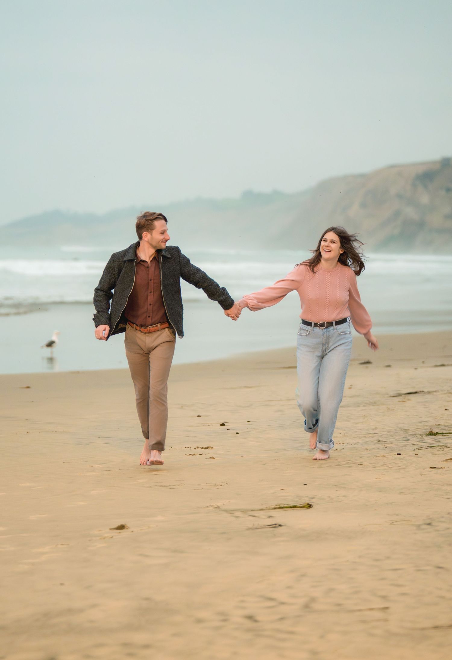 Couple running along shoreline during a playful outdoor engagement photography session captured by a Colorado couples photographer.