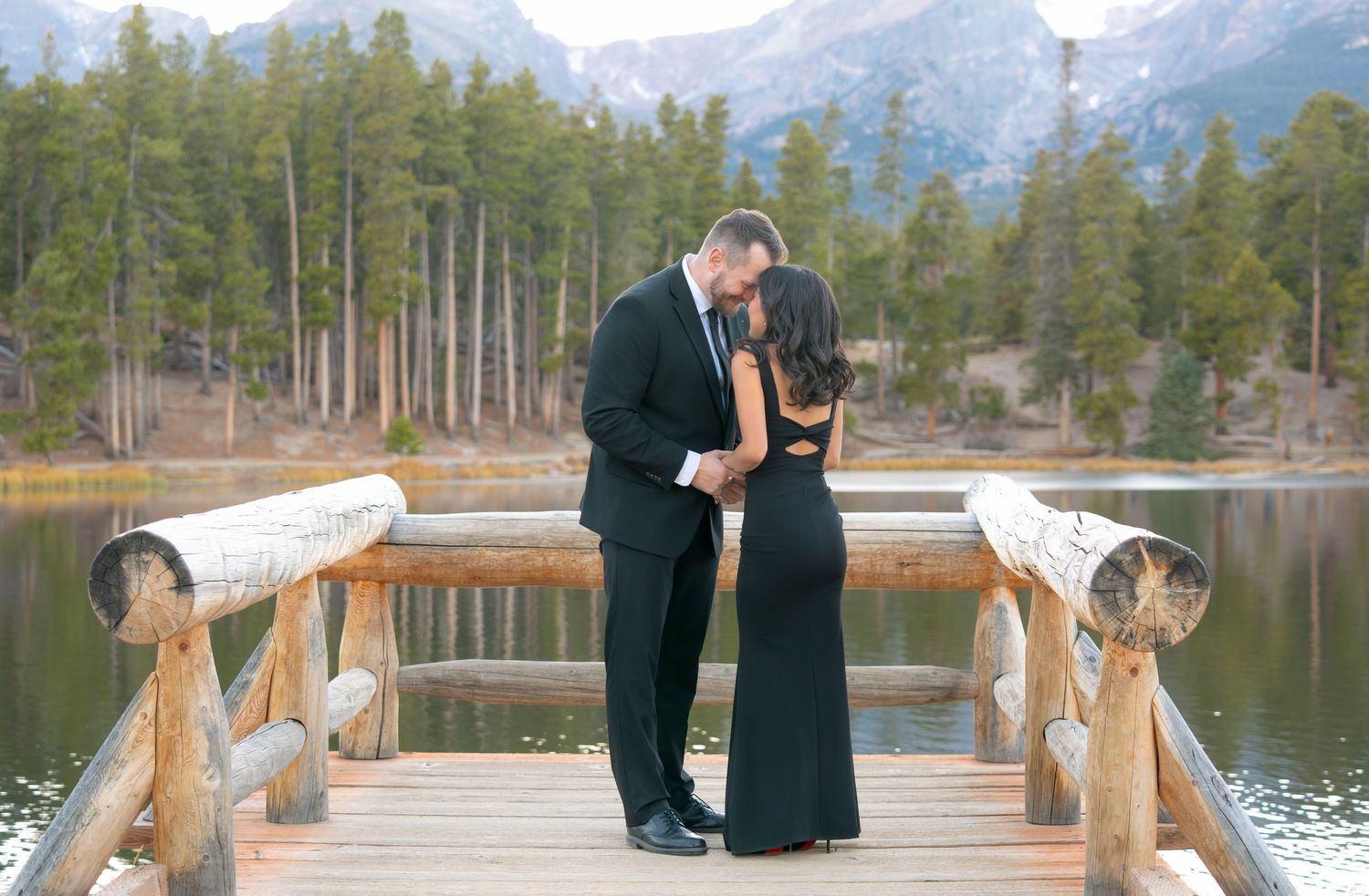 Couple embracing on dock at Sprague Lake in Estes Park during a romantic Rocky Mountain National Park engagement photography session.