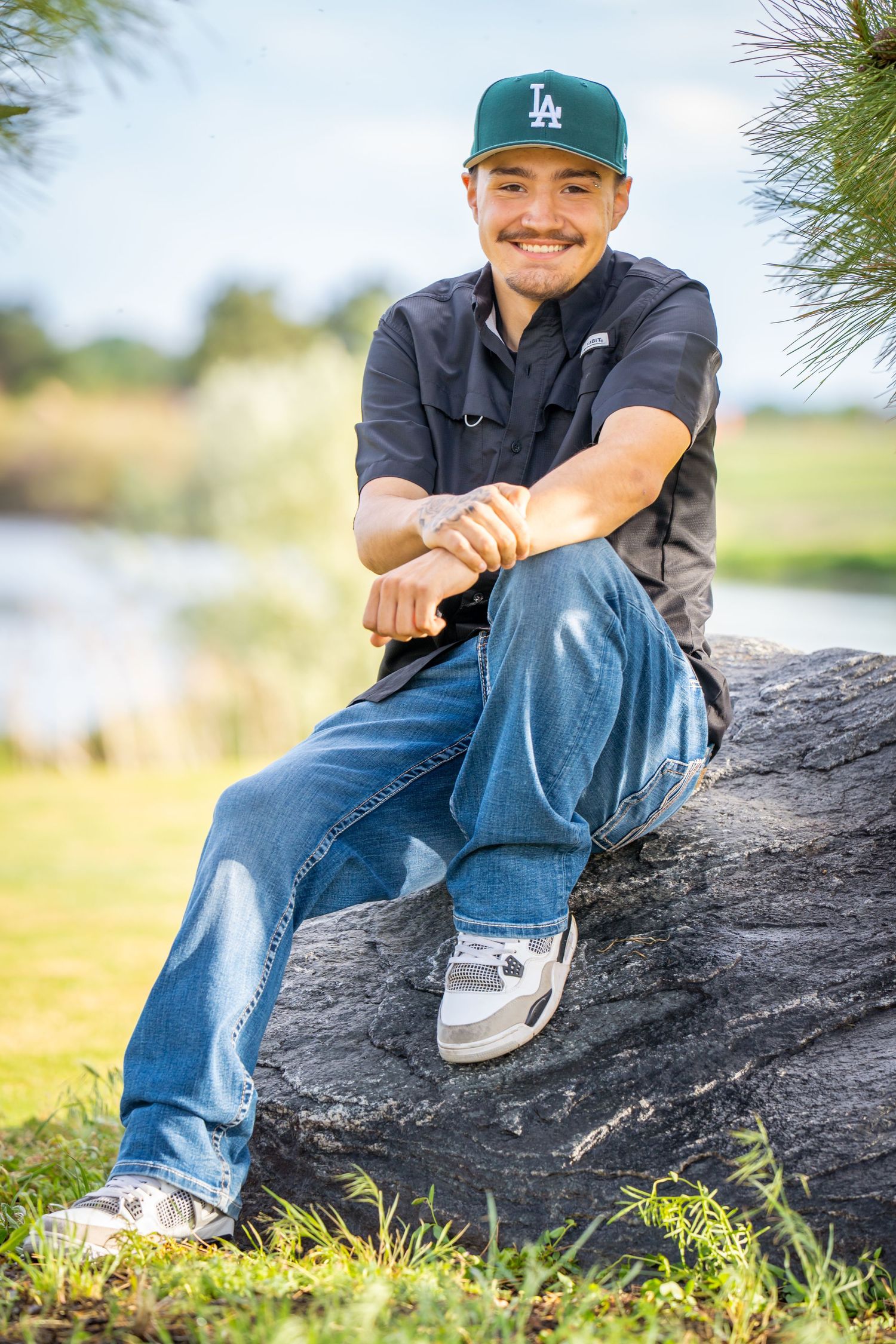 High school senior sitting on rock near water during an outdoor senior portrait session captured by a Denver area senior photographer.