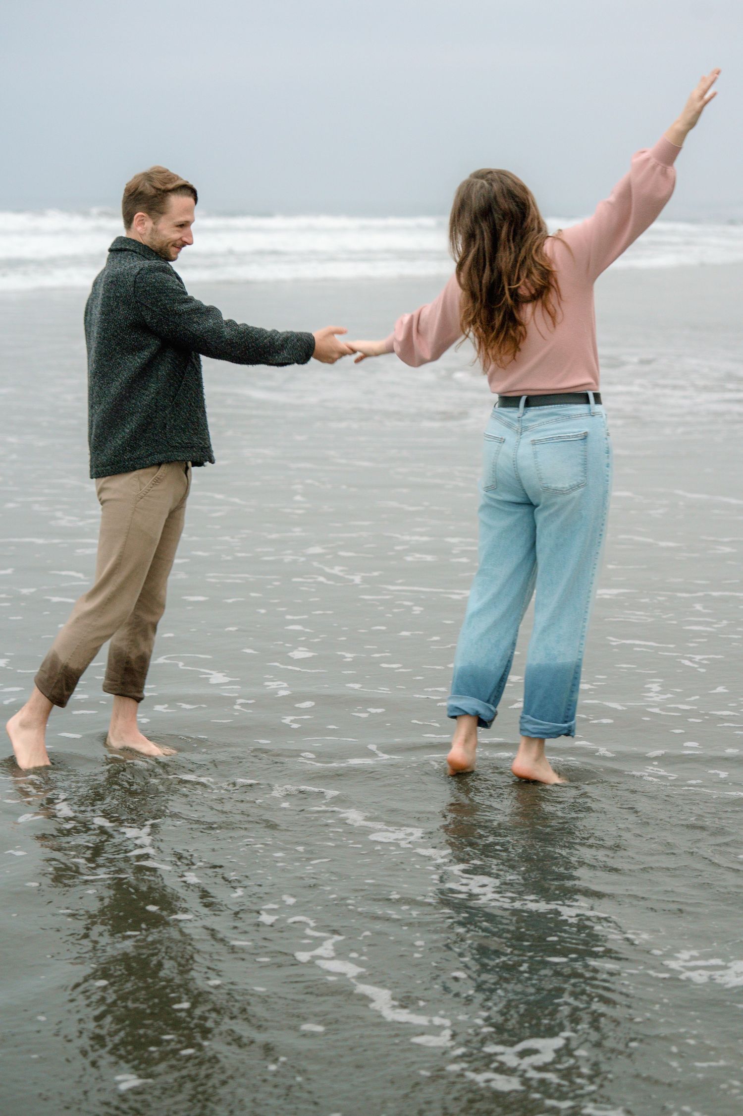 Playful couple dancing in ocean waves during a natural beach engagement photography session captured by a Colorado couples photographer.
