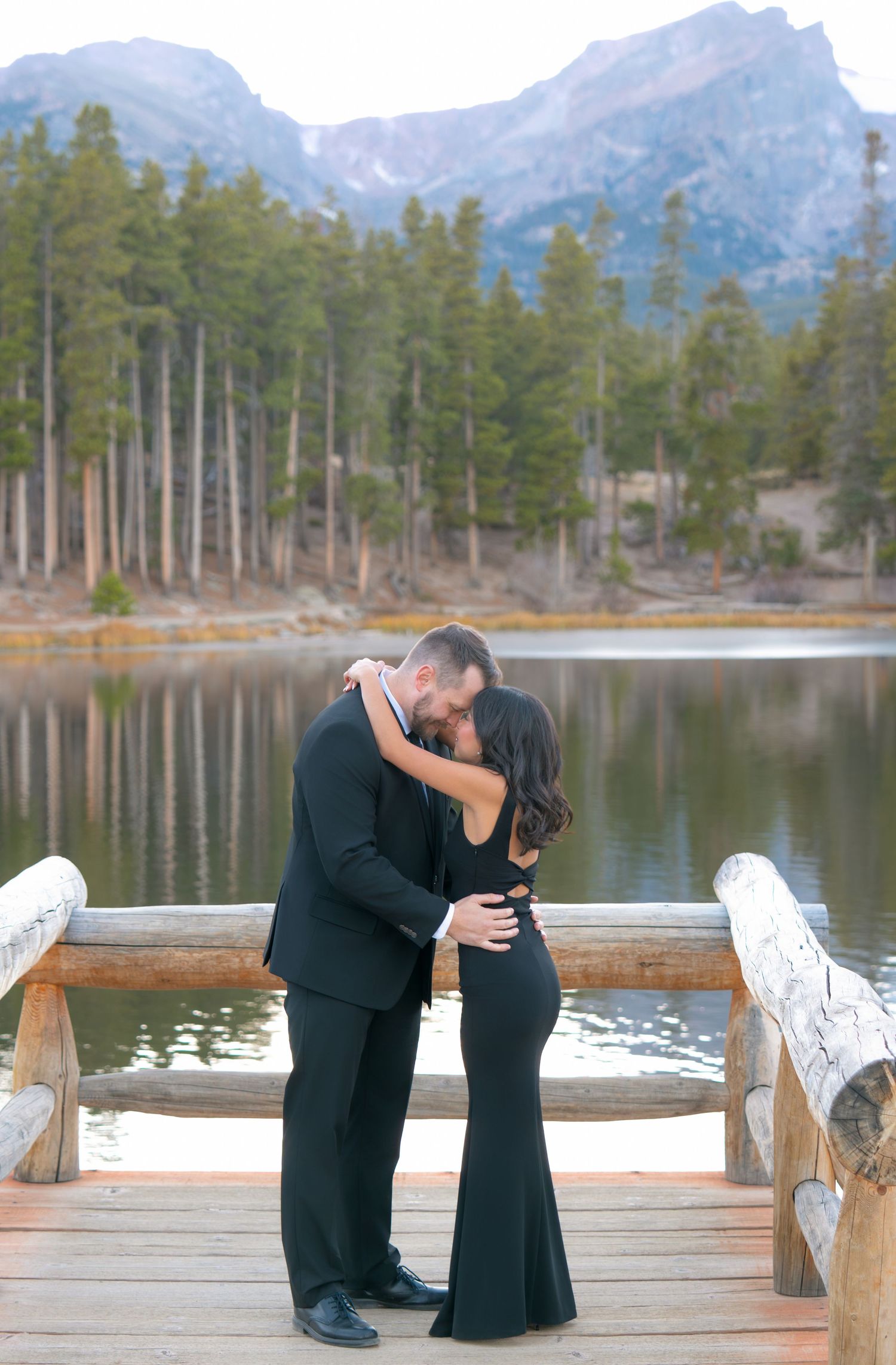 Couple kissing on wooden dock with mountain Sprague Lake backdrop during  romantic Colorado engagement photography session in the mountains.