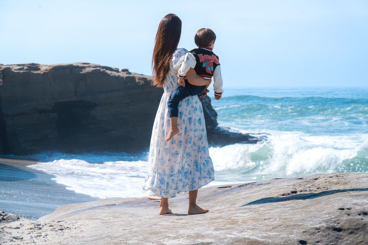 Mother holding child while looking at ocean waves during a relaxed outdoor family portrait session by a Denver area family photographer.