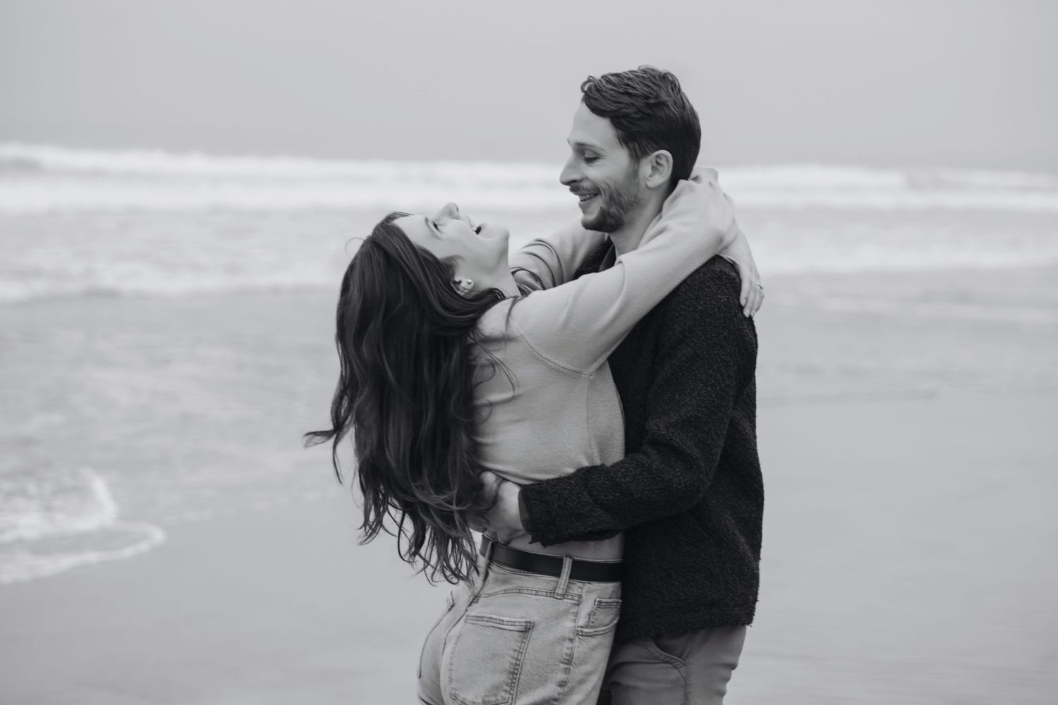 Fun happy couple embracing by the ocean during a natural outdoor engagement photography session captured by a Colorado photographer.