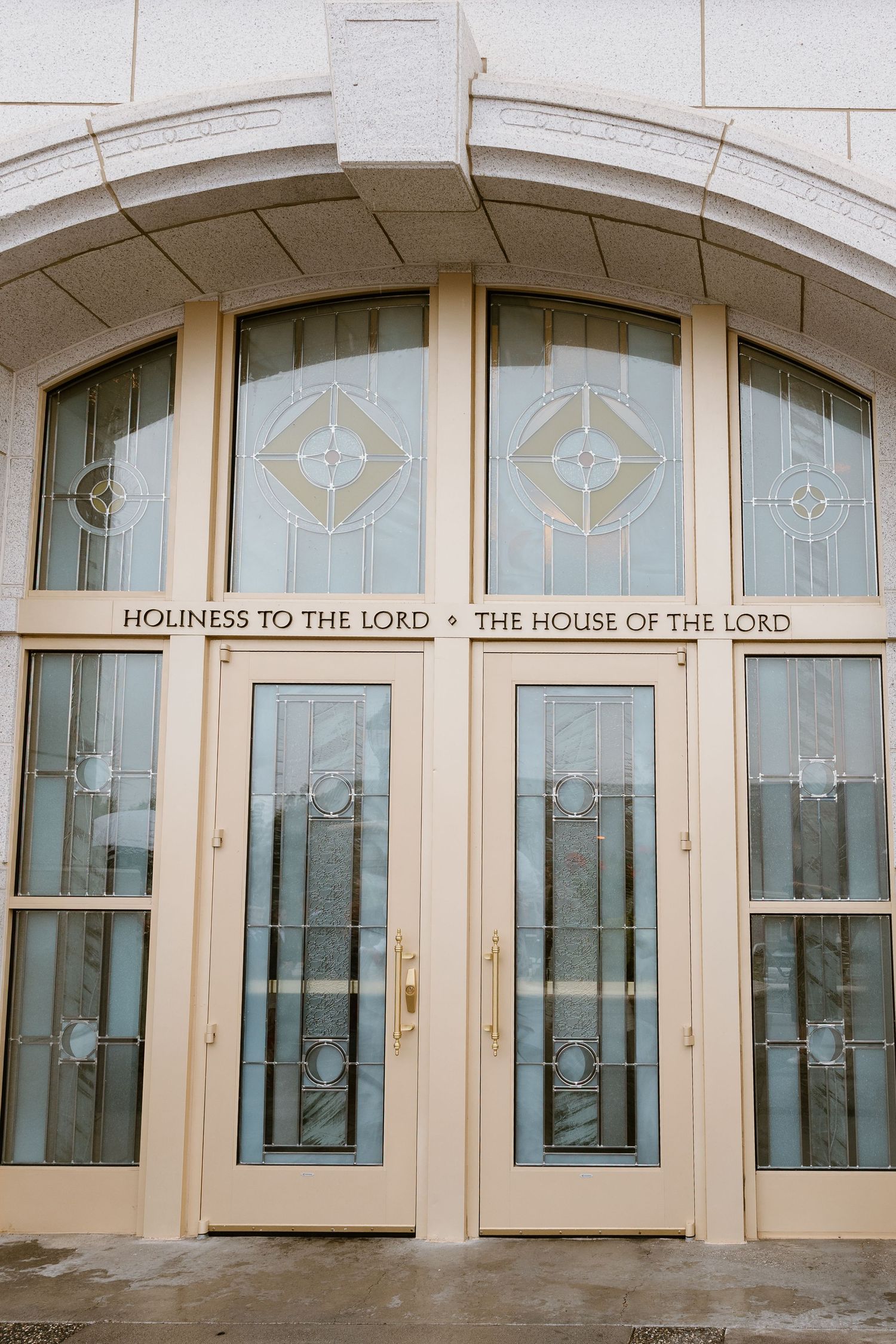 Architectural detail showing arched glass doors and windows with 'Holiness to the Lord - The House of the Lord' text above.
