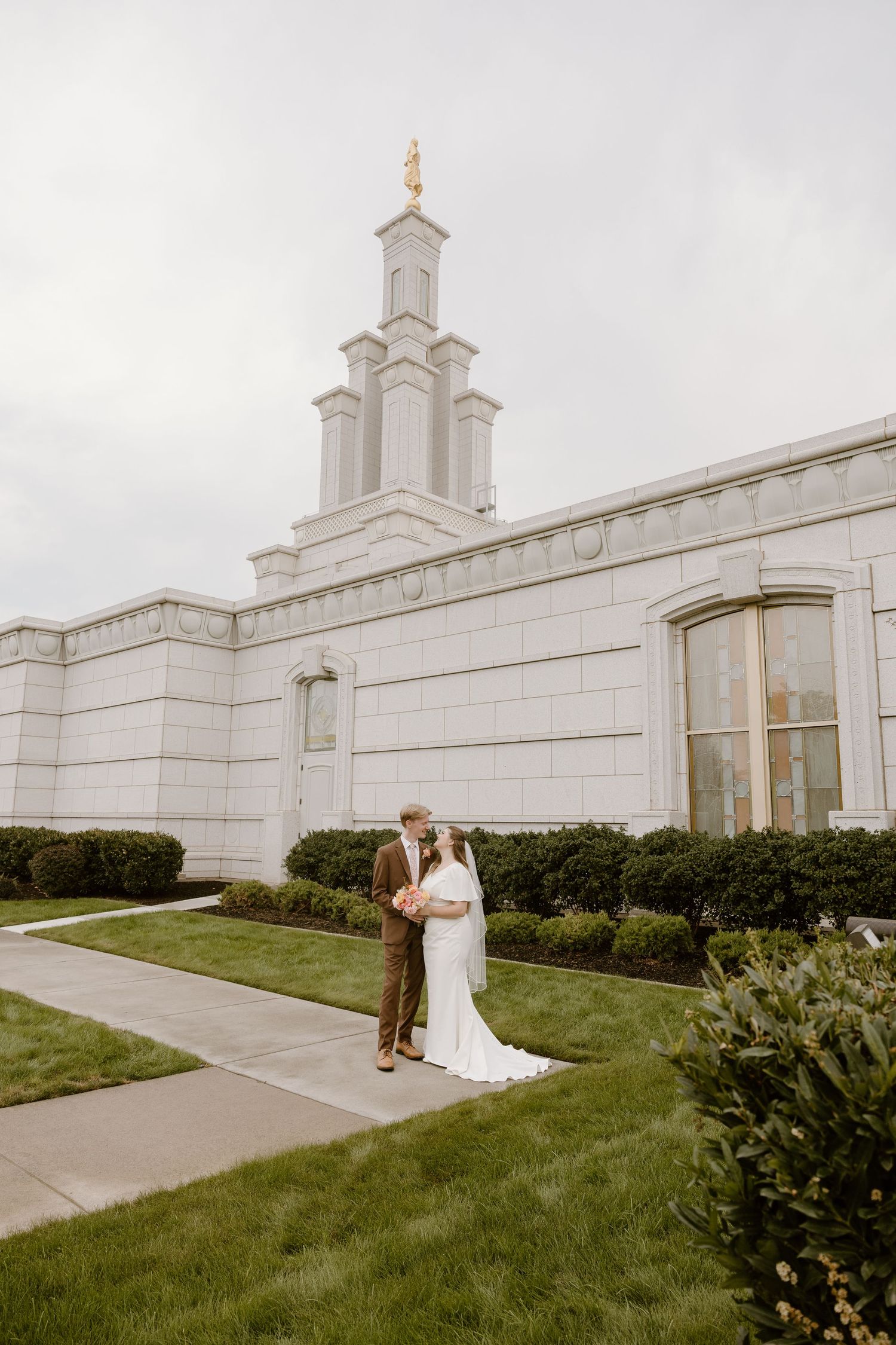 Wedding couple poses together on the grounds of a white Mormon temple with elegant architecture and landscaping.