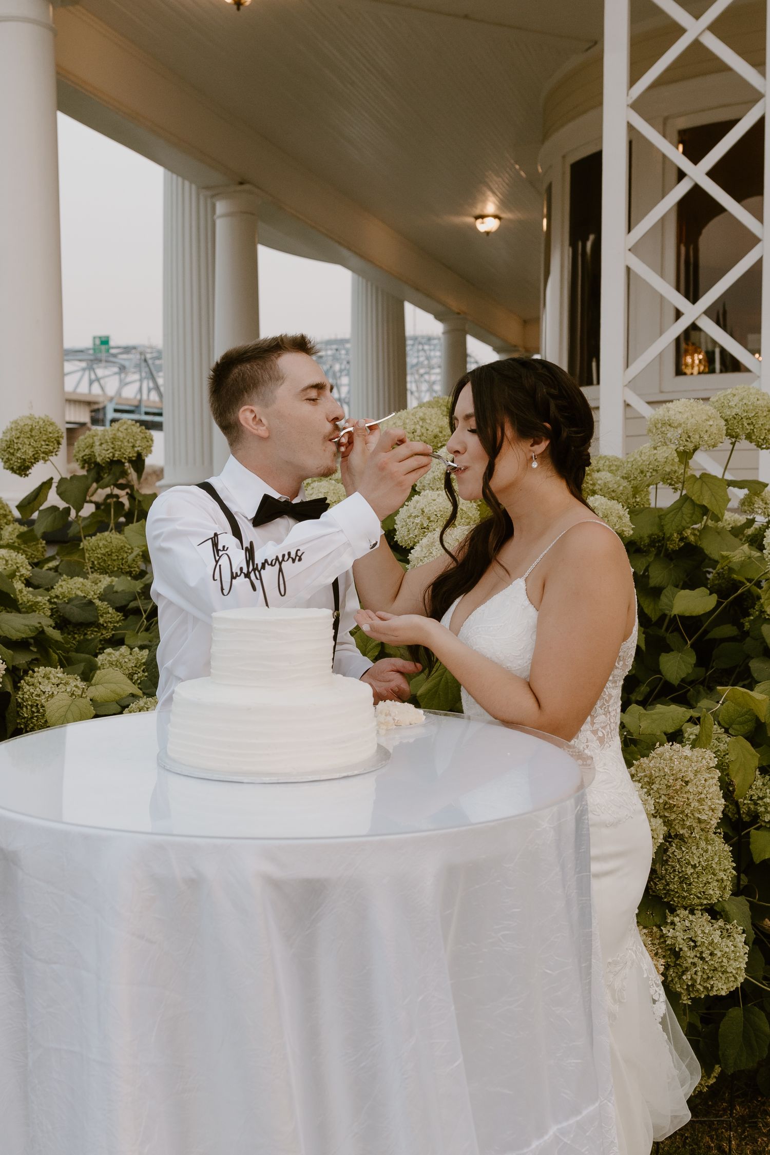 Bride and groom share a playful moment while feeding each other wedding cake at an elegant outdoor reception.