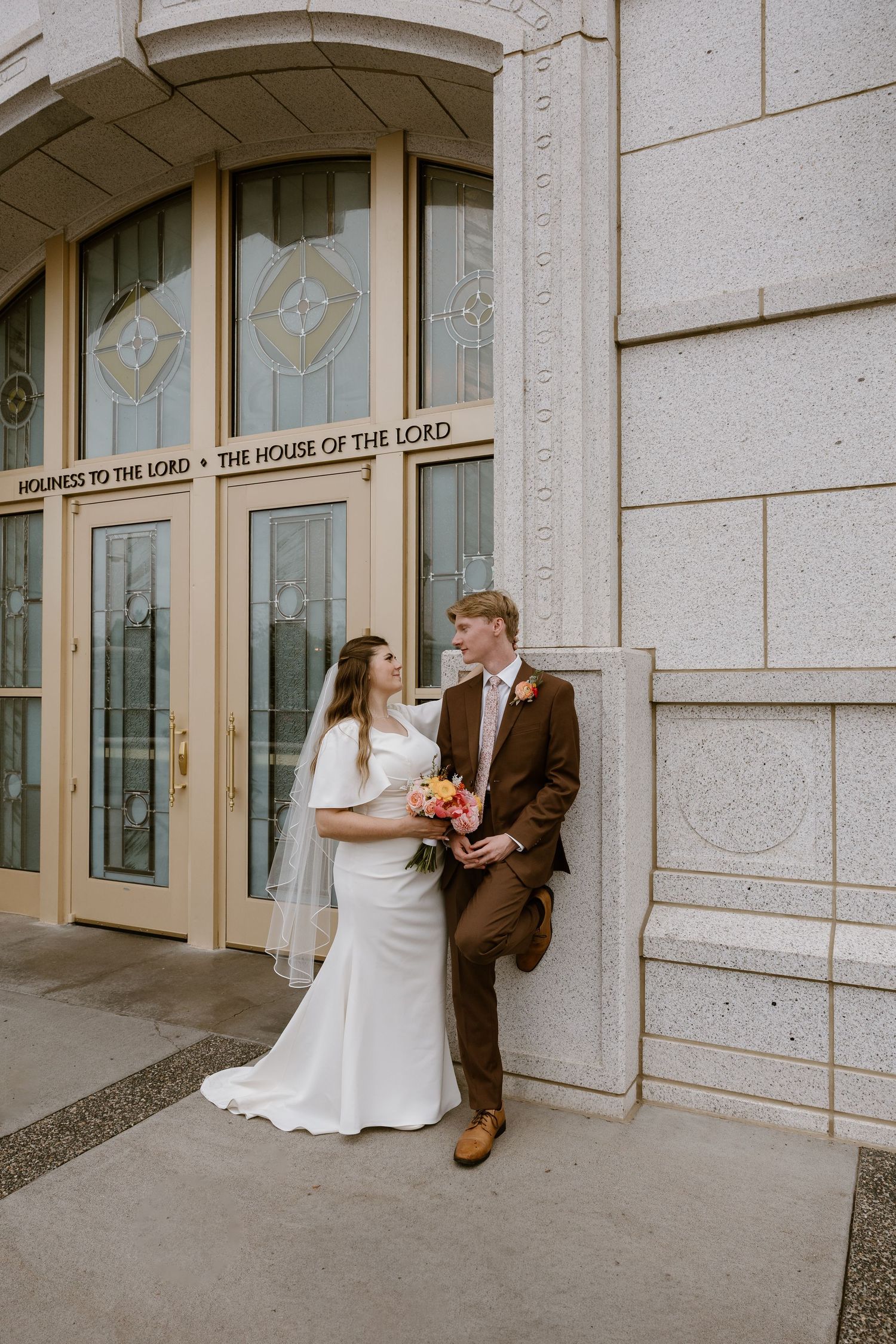 A couple shares a romantic moment outside a stone building with 'House of the Lord' text visible in the window.