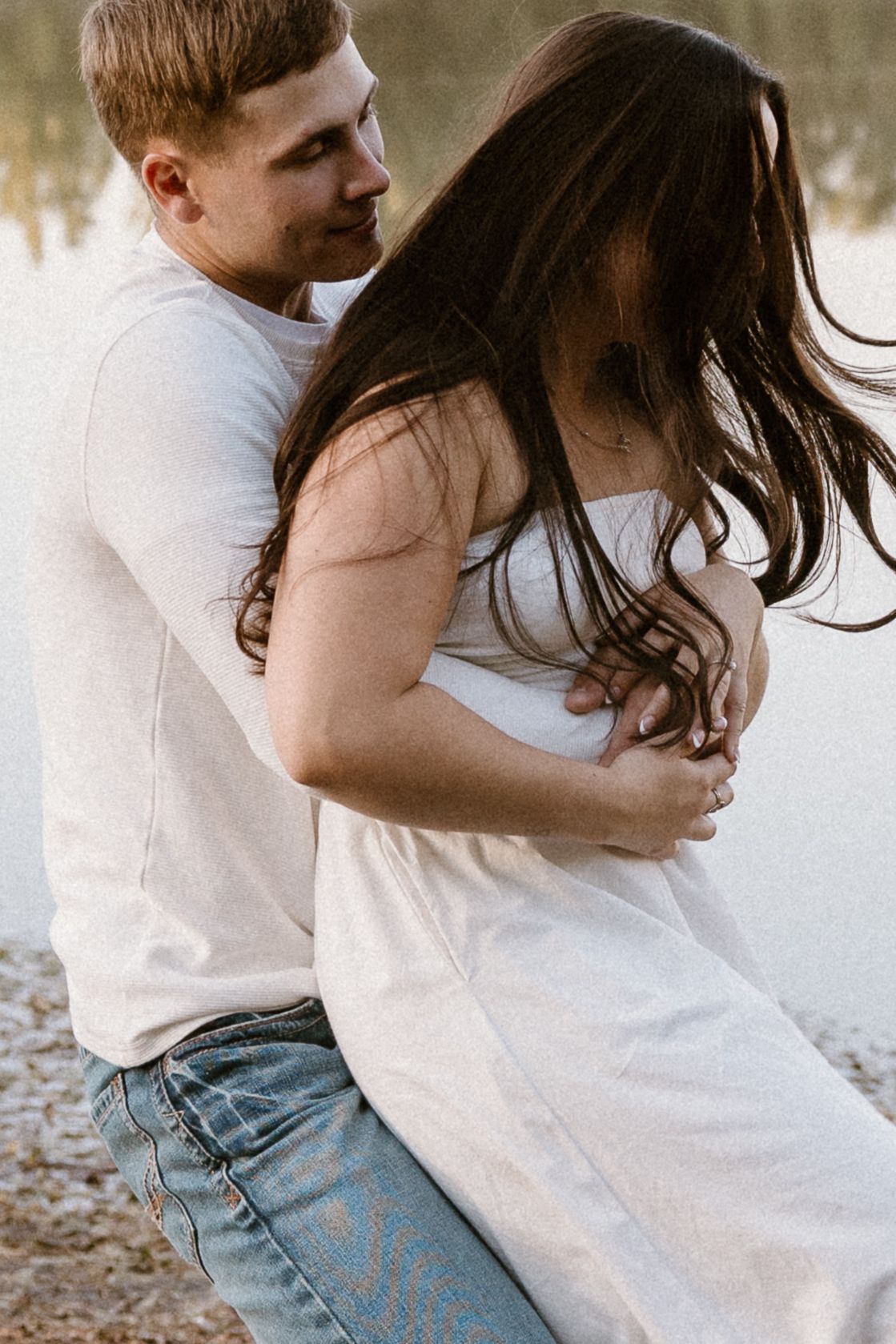 A couple embraces intimately in a romantic outdoor photoshoot series showing tender moments by a lake.