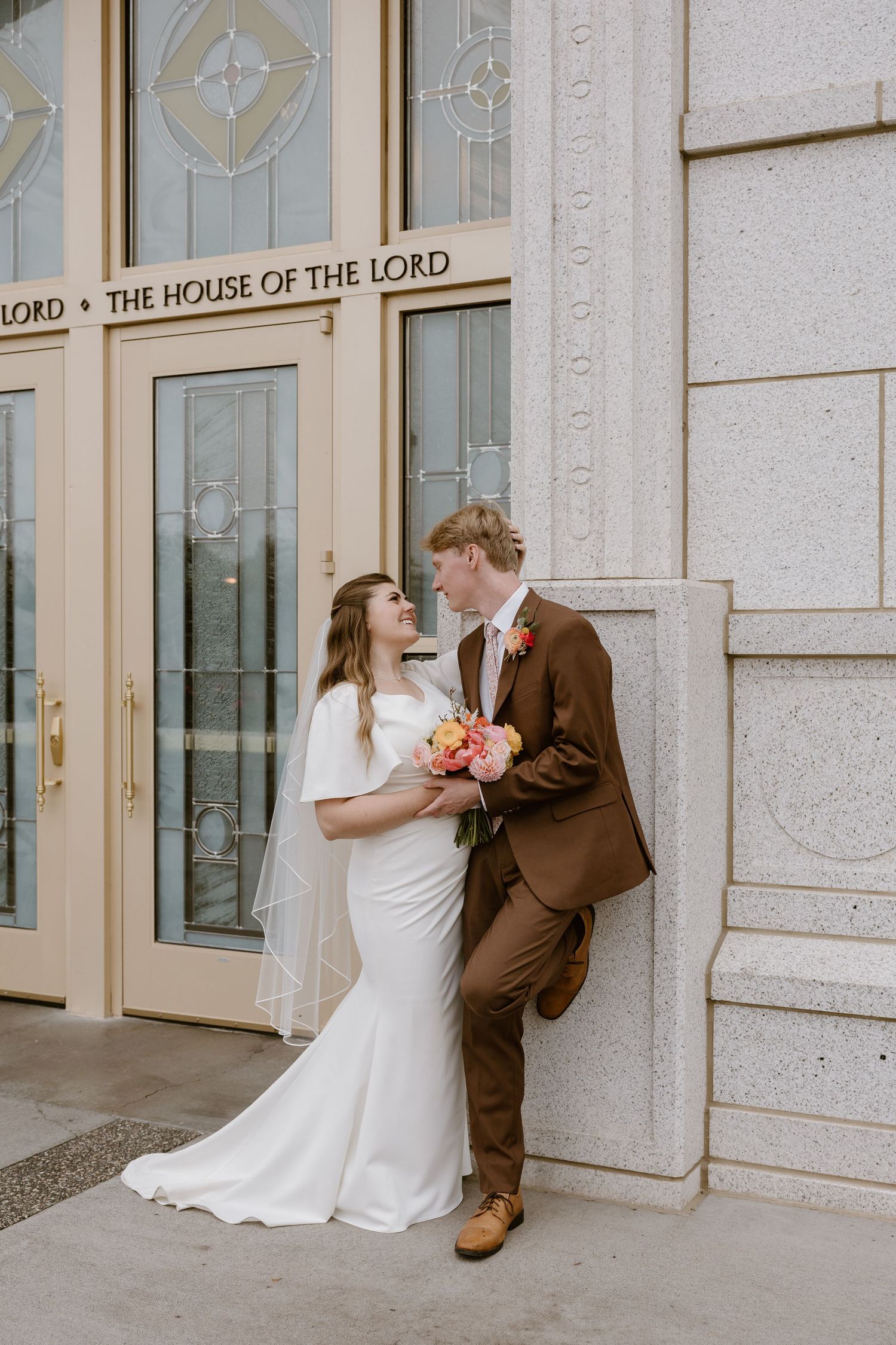 A romantic wedding couple shares playful moments in front of a church entrance with 'House of the Lord' signage.