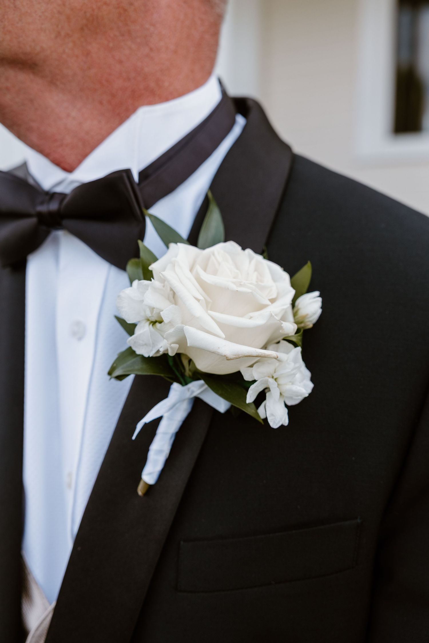 A black suit lapel adorned with white rose and baby's breath boutonnieres for a formal wedding.