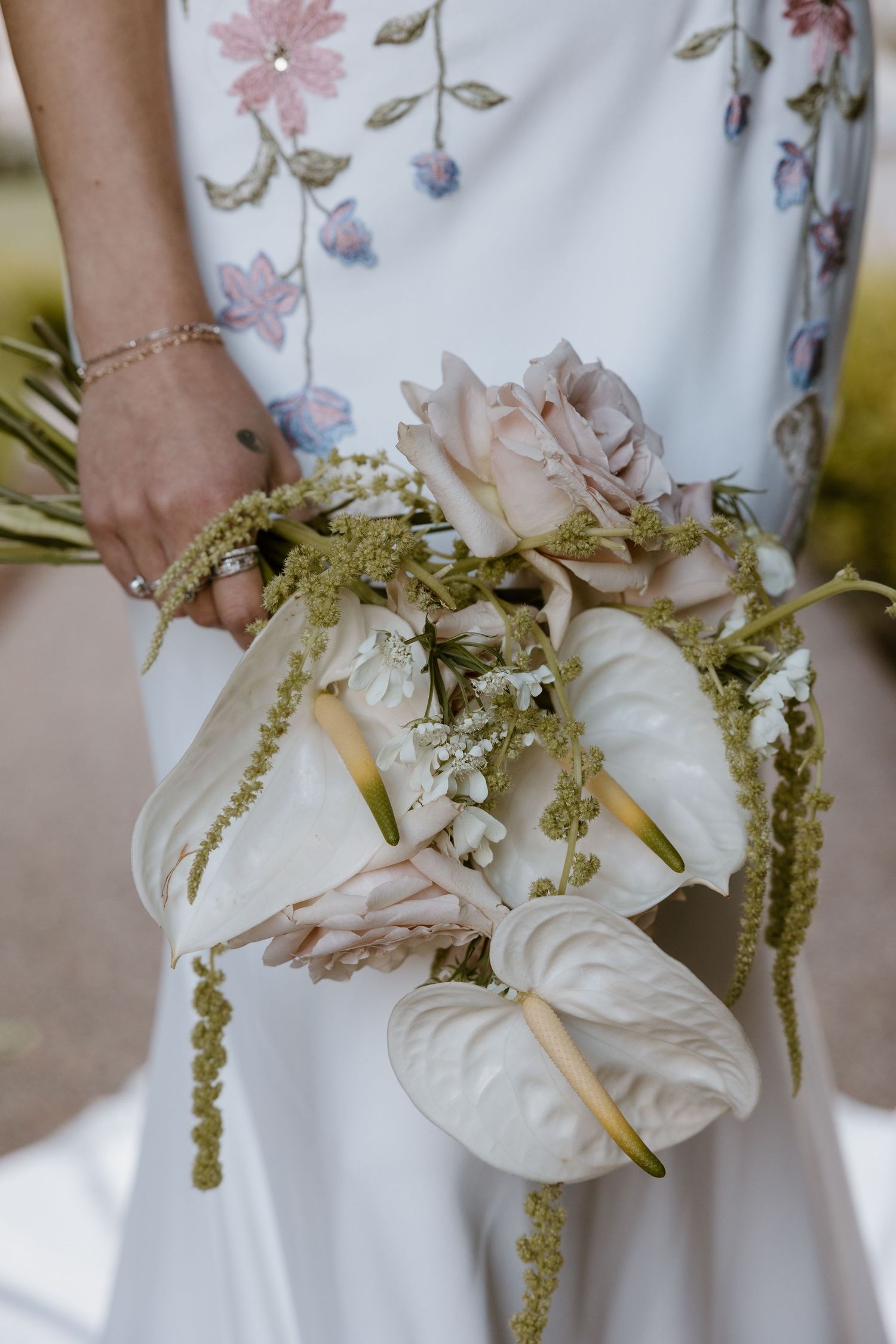 Close-up view of a white wedding bouquet with cascading amaranthus and delicate floral details against a floral dress.