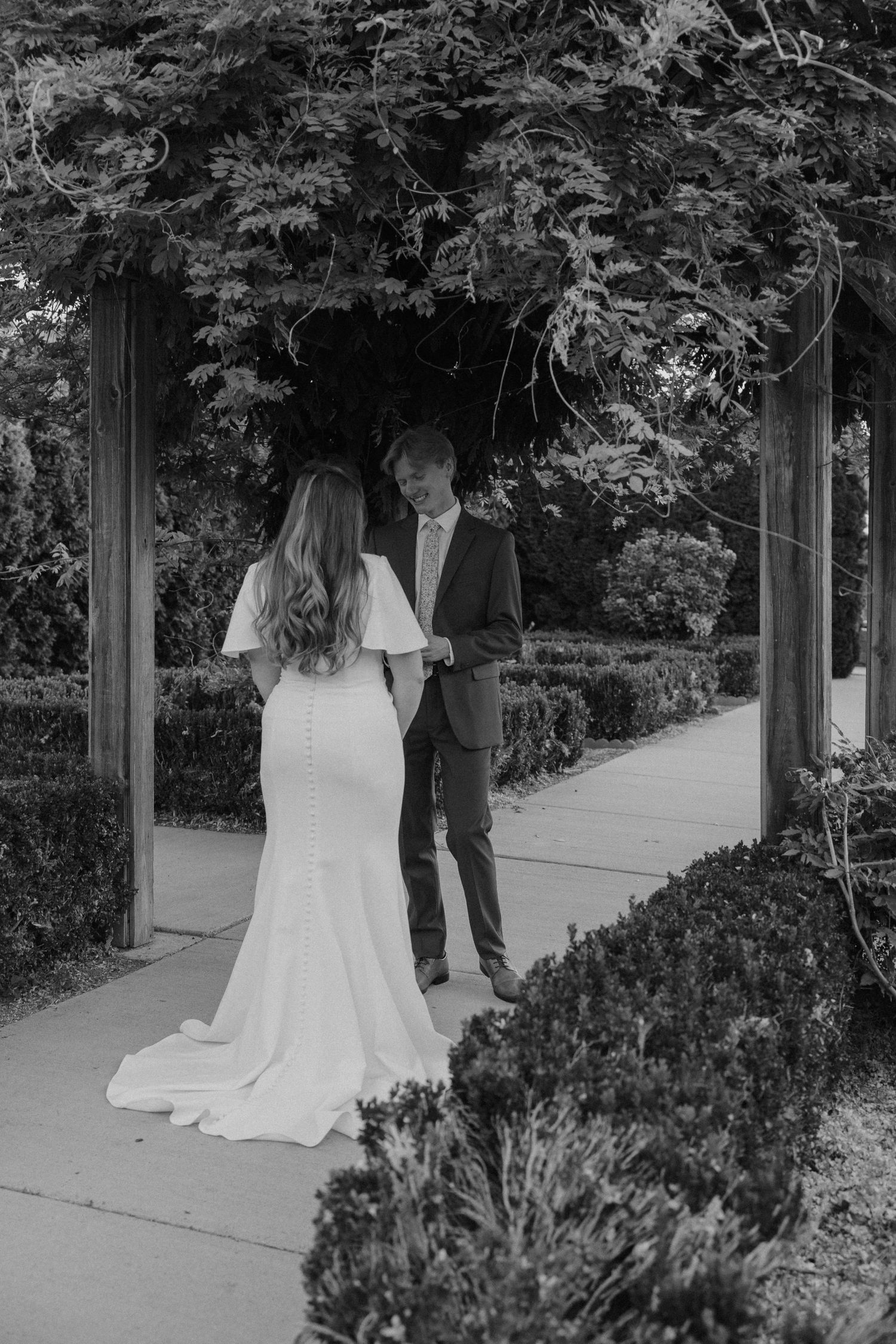 A romantic black and white wedding photo of a couple standing under a lush garden archway.