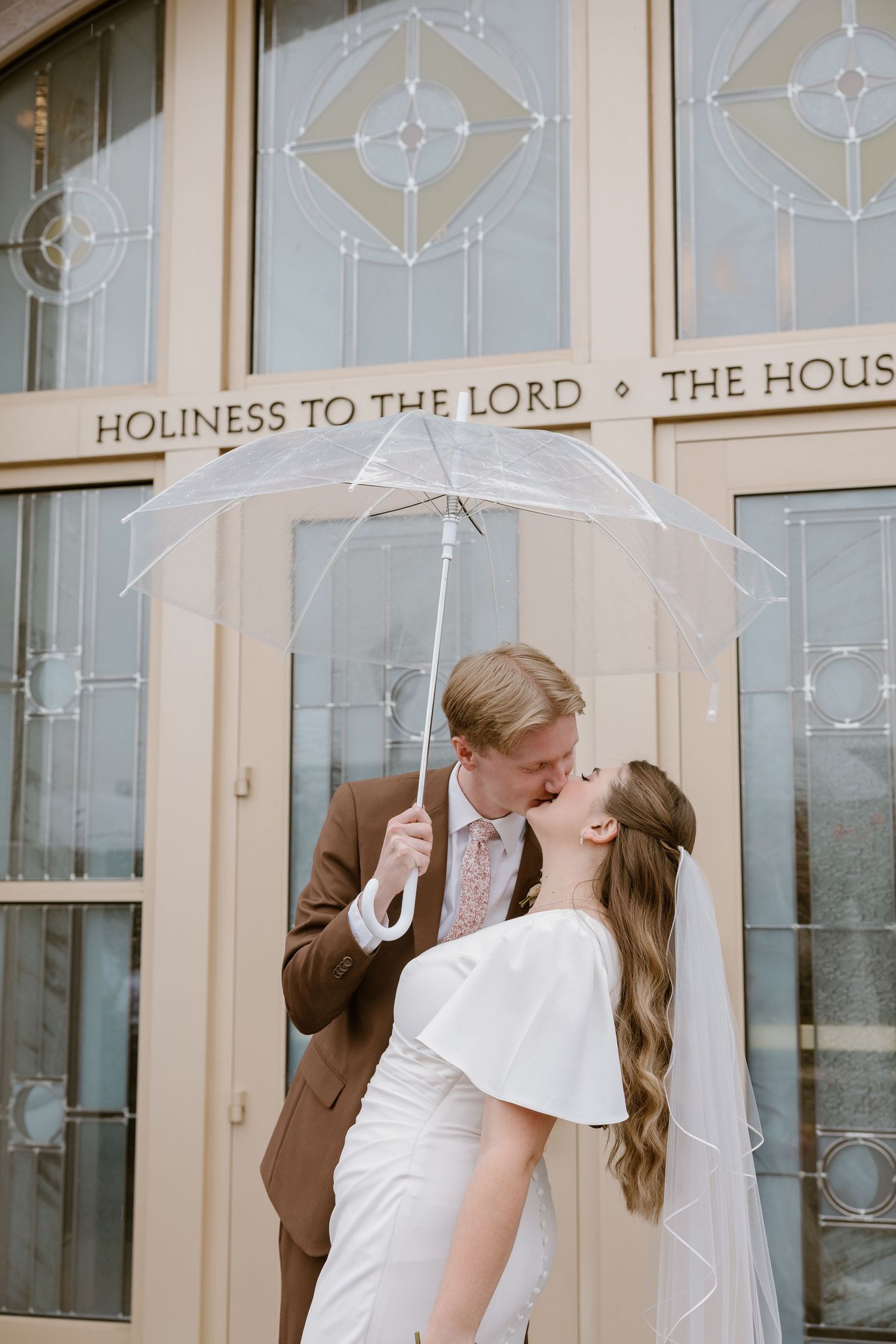 A couple shares a tender moment in front of stained glass windows at a church wedding ceremony.