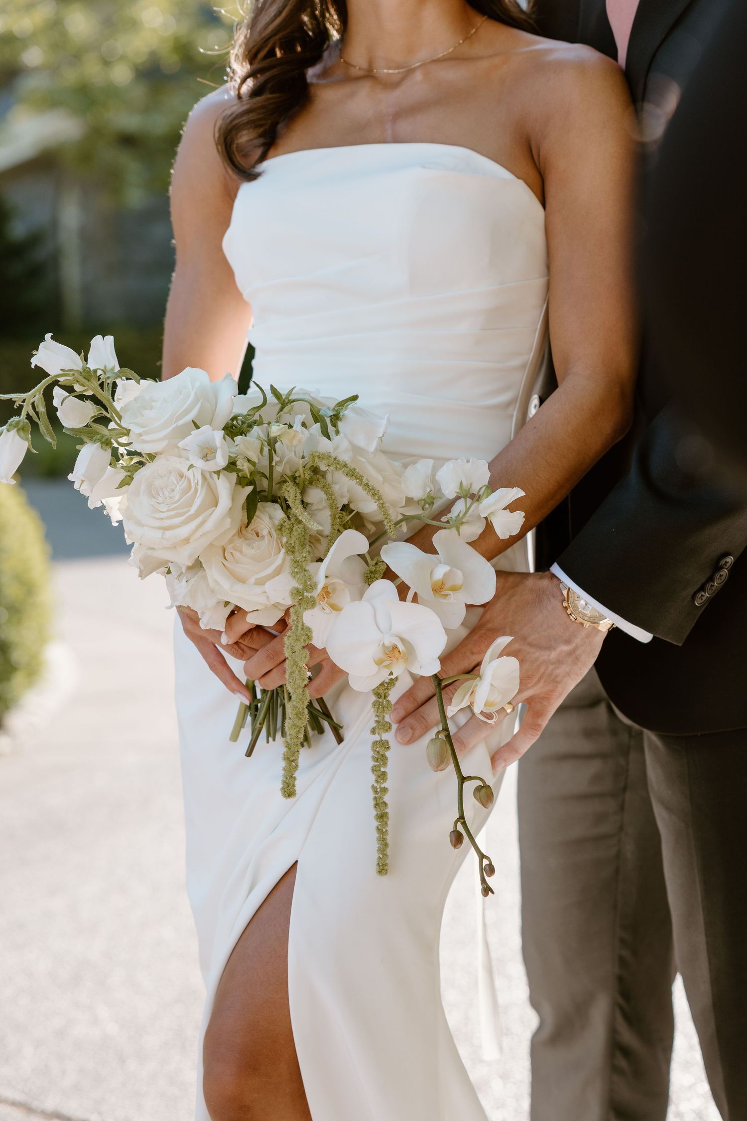 Wedding bouquet of white orchids and roses held against a white bridal gown in natural outdoor lighting.