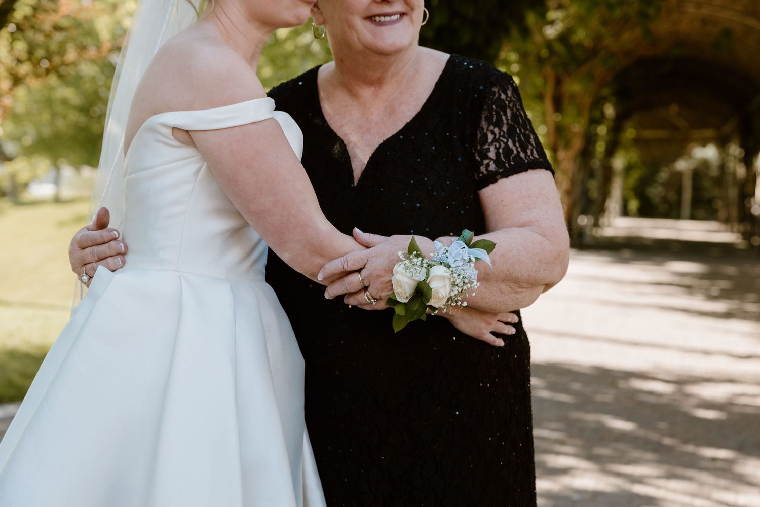 Two people embrace at a wedding ceremony, with one wearing a white bridal gown and another in a black lace dress.