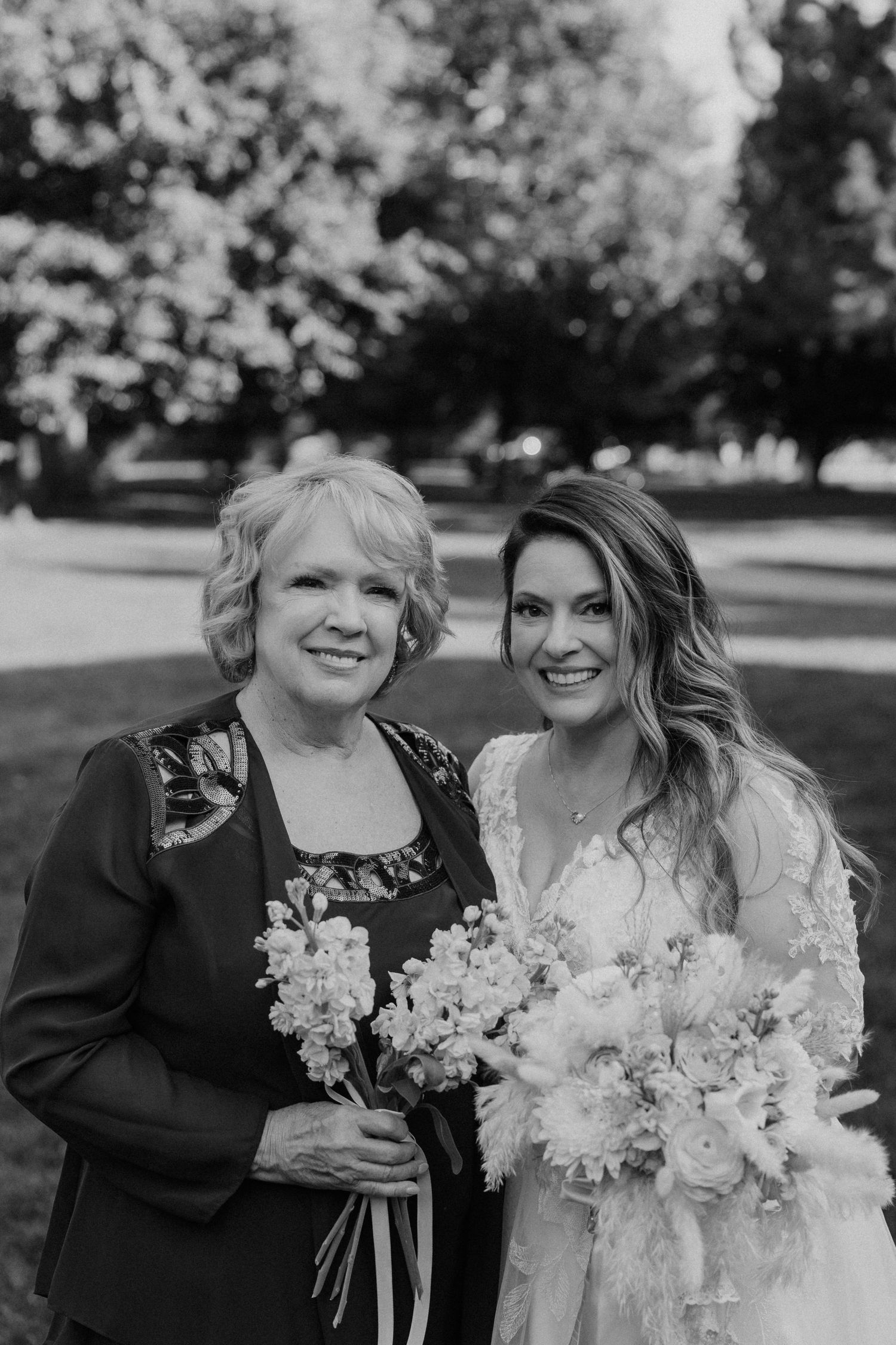 Black and white photo of two people at a wedding holding beautiful floral bouquets outdoors.