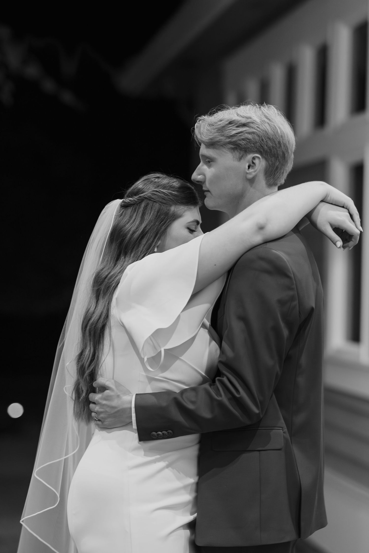 A romantic black and white portrait of newlyweds sharing an intimate embrace outdoors.