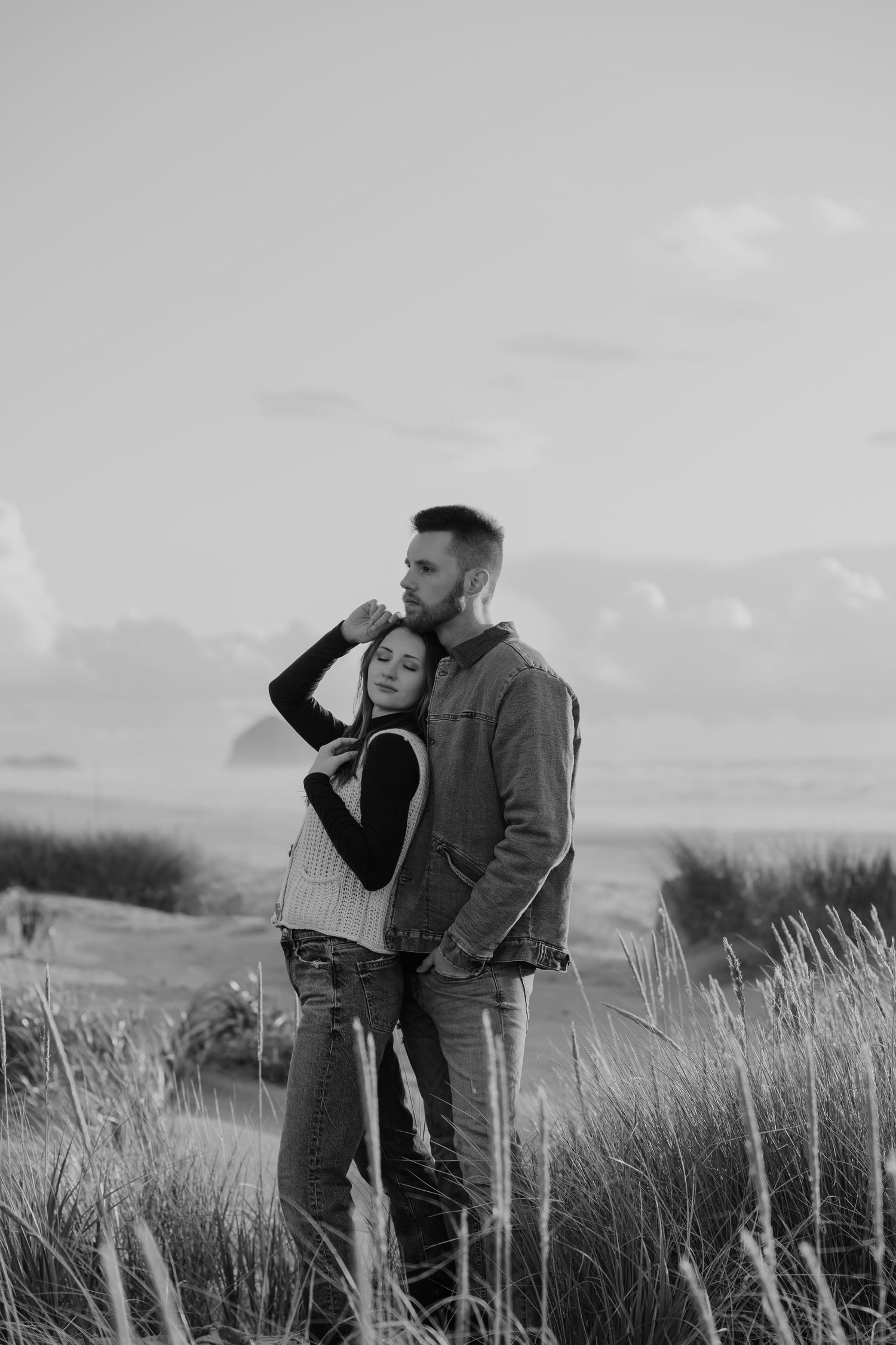 Black and white photo shows a couple in a grassy field against a cloudy sky.